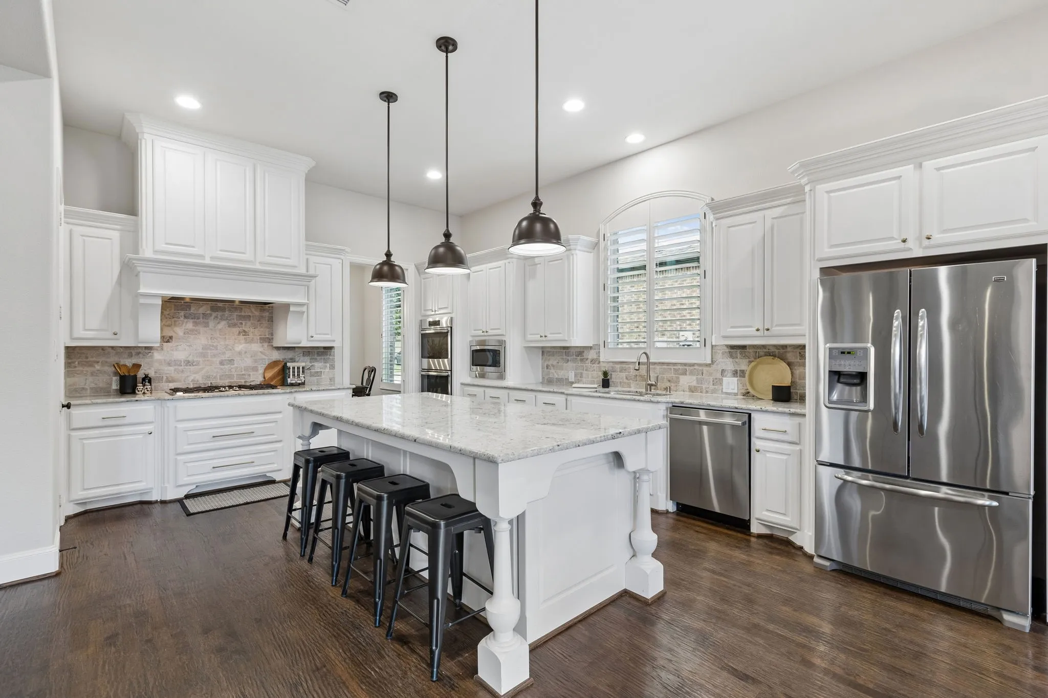 Kitchen featuring white shaker-style cabinetry, stone countertops, brick-style backsplash, stainless steel appliances, and wood-finish flooring
