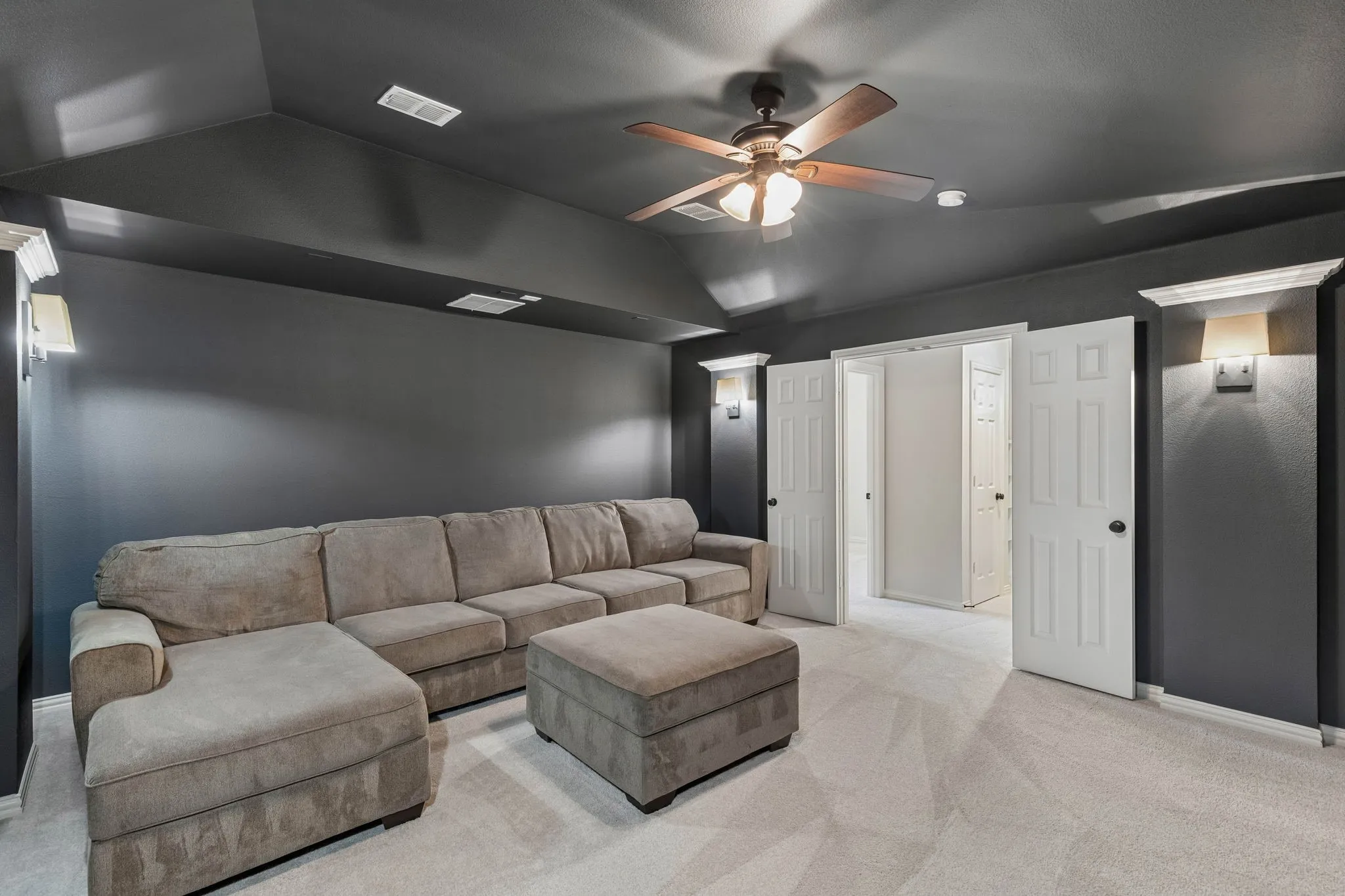 Vaulted ceiling featuring a central multi-blade ceiling fan with integrated lighting, wall-mounted light fixtures, and double doors