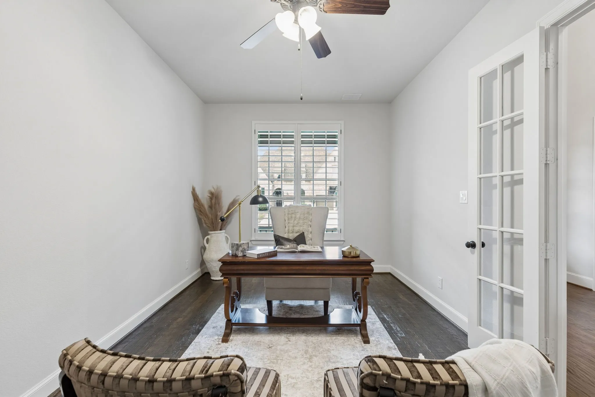 Wood-finish flooring, white French doors with glass panes, plantation shutters, and a ceiling fan with light fixture