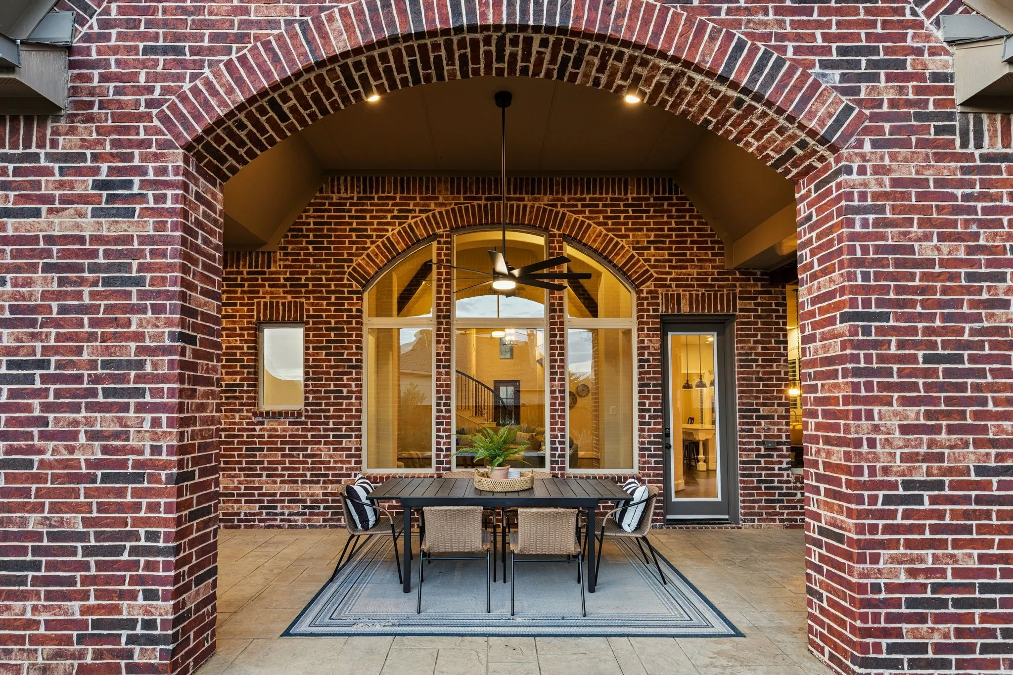 Covered patio featuring red brick masonry, a vaulted ceiling, arched architectural detailing, a central ceiling fan, and large multi-pane windows