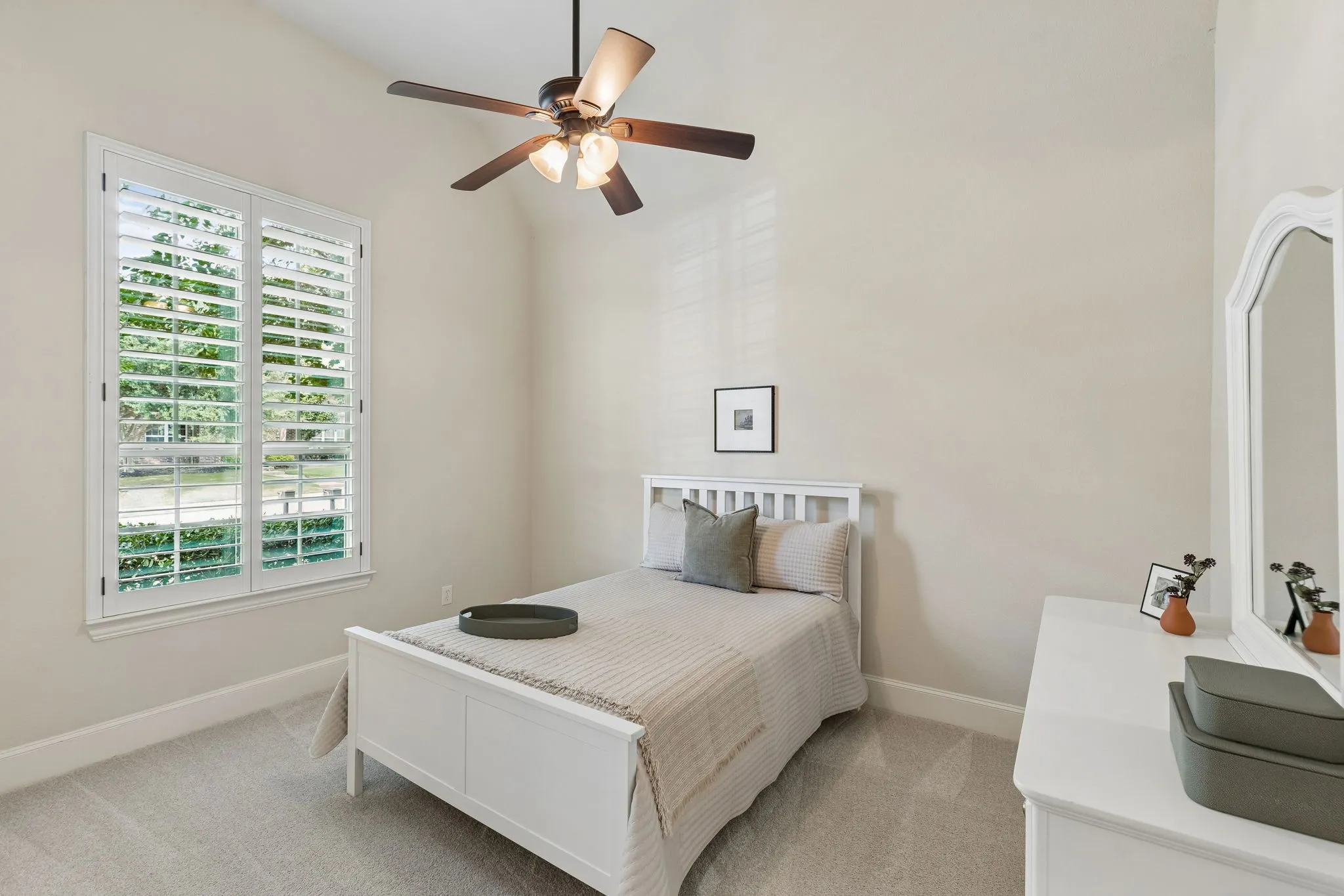 Vaulted ceilings, carpeted flooring, and plantation shutters featuring adjustable louvers, complemented by a multi-blade ceiling fan with integrated lighting