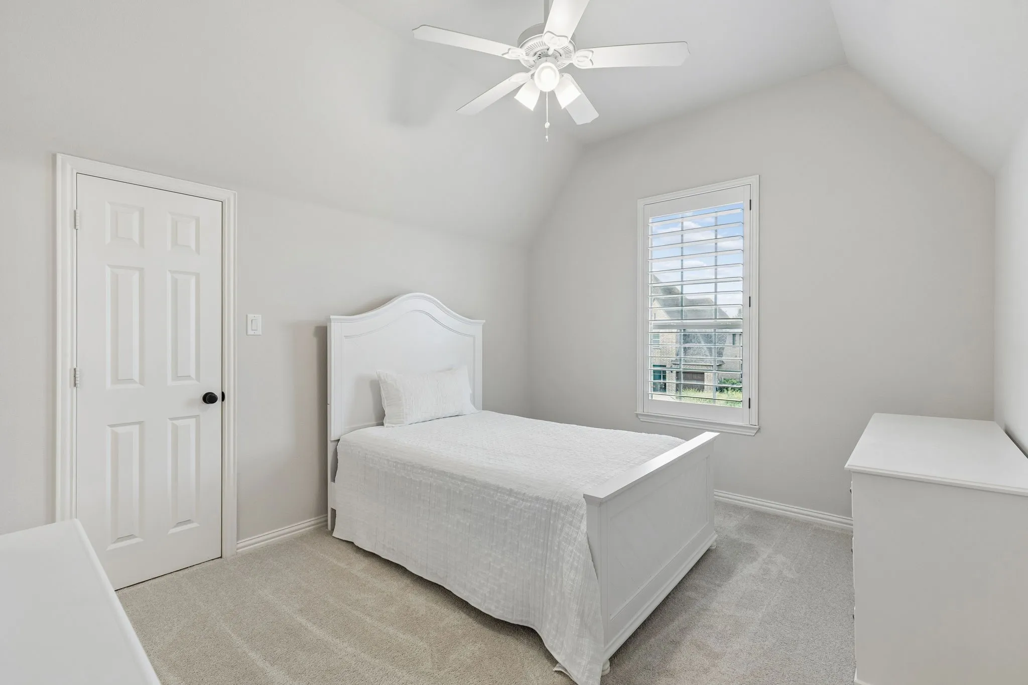 Vaulted ceiling featuring a ceiling fan with integrated lighting, wall-to-wall carpeting, and a window with plantation-style shutters