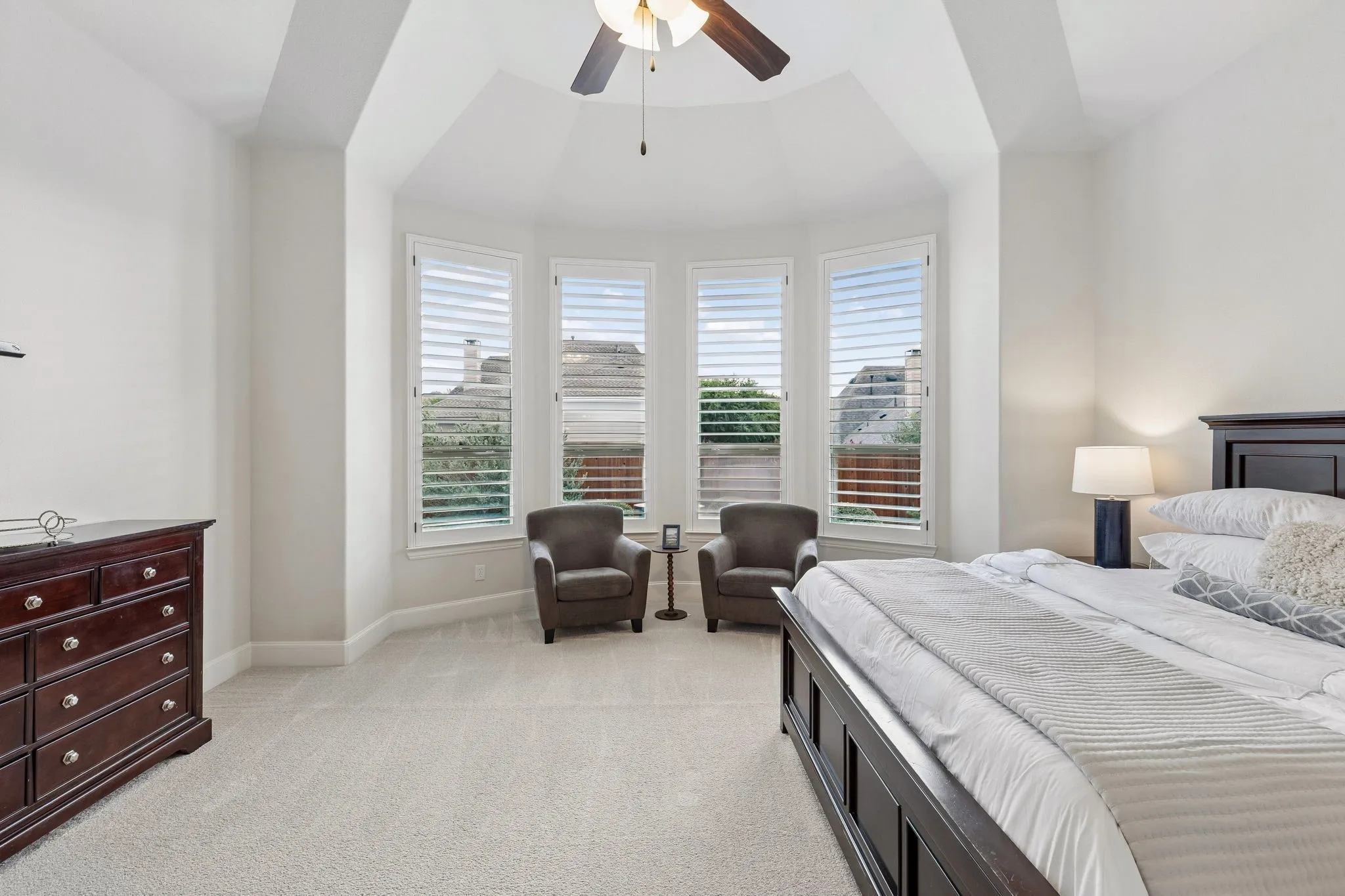 Tray ceiling, bay window with plantation shutters, and ceiling fan