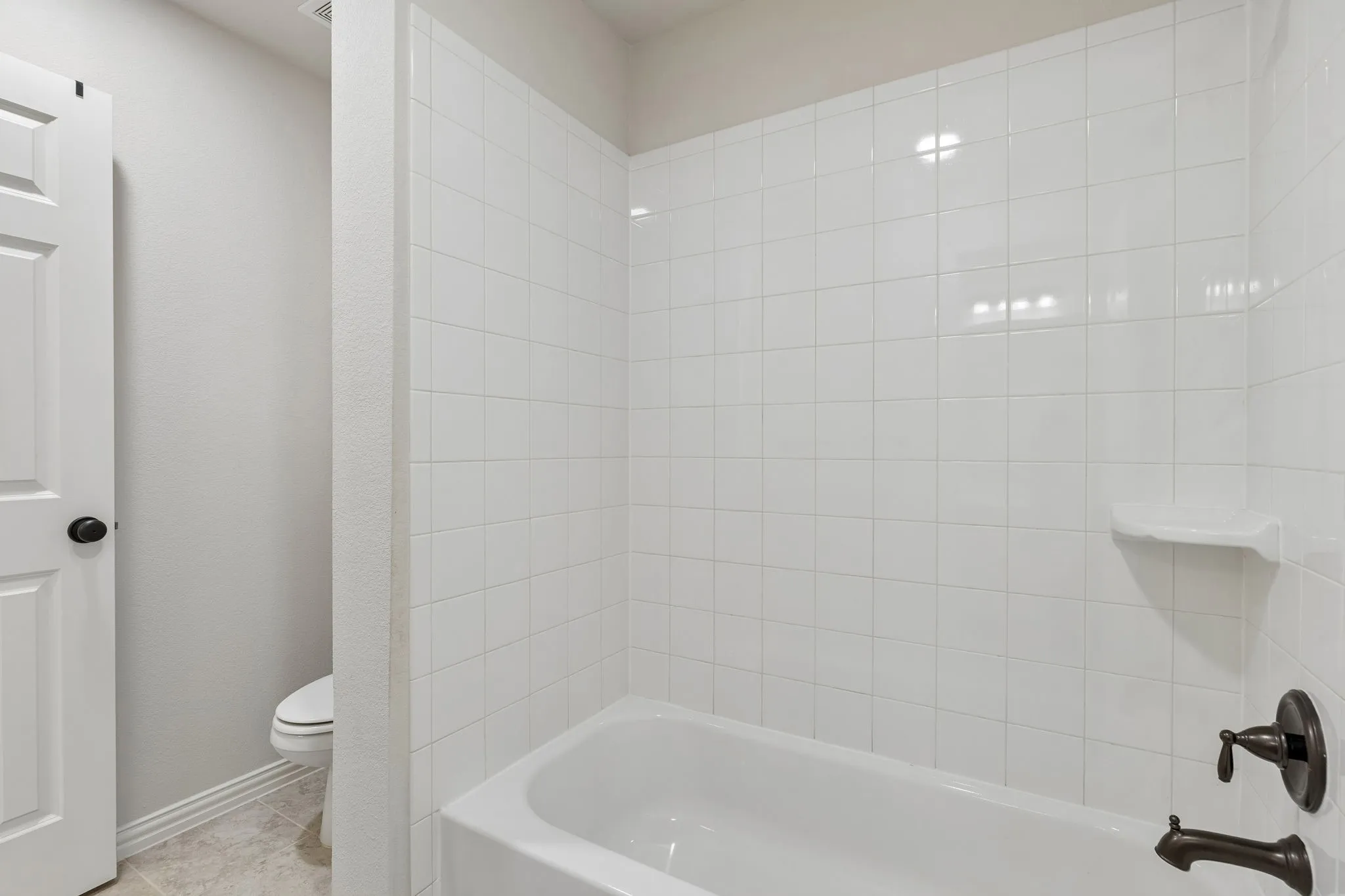 Bathtub enclosure featuring white square tile surround, built-in soap niche, and oil-rubbed bronze faucet hardware