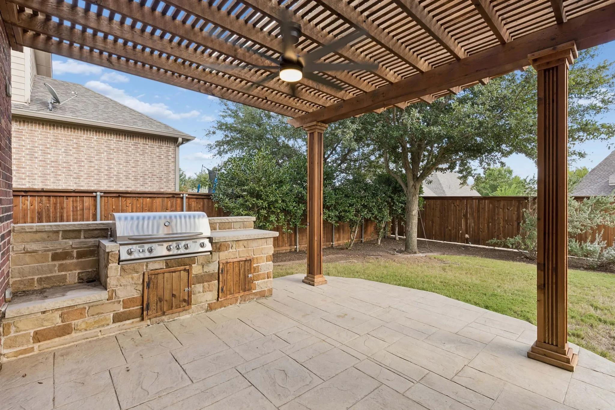 Covered patio featuring a timber pergola with a ceiling fan, stone-surround built-in grill, and stamped concrete flooring
