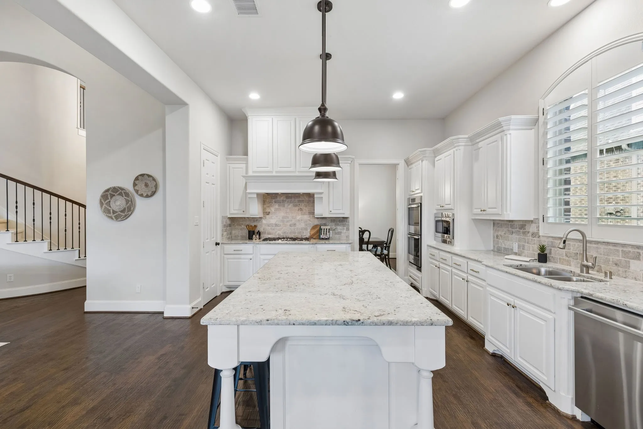 Kitchen featuring a central island with stone countertop, white cabinetry, integrated stainless steel appliances, brick-patterned tile backsplash, and dark wood-finish flooring