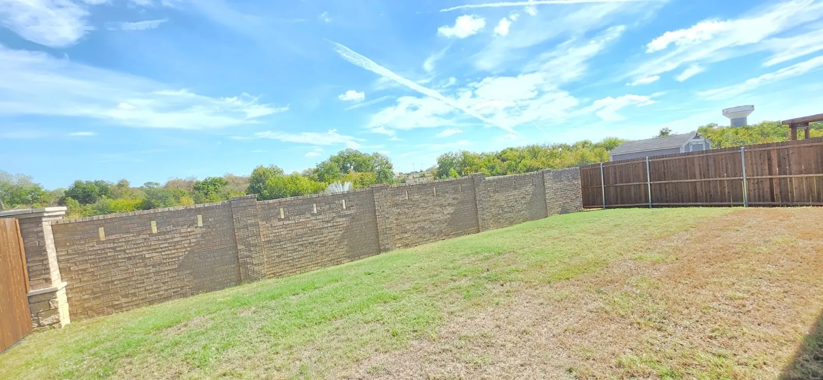 Expansive backyard featuring a stone retaining wall, wood privacy fencing, and a grassy area