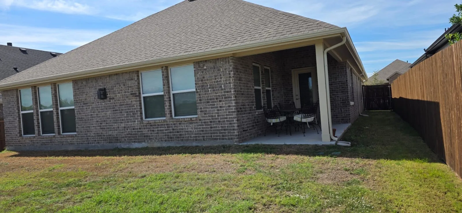 Brick exterior with a covered patio, neutral-toned roofing, and a wooden privacy fence