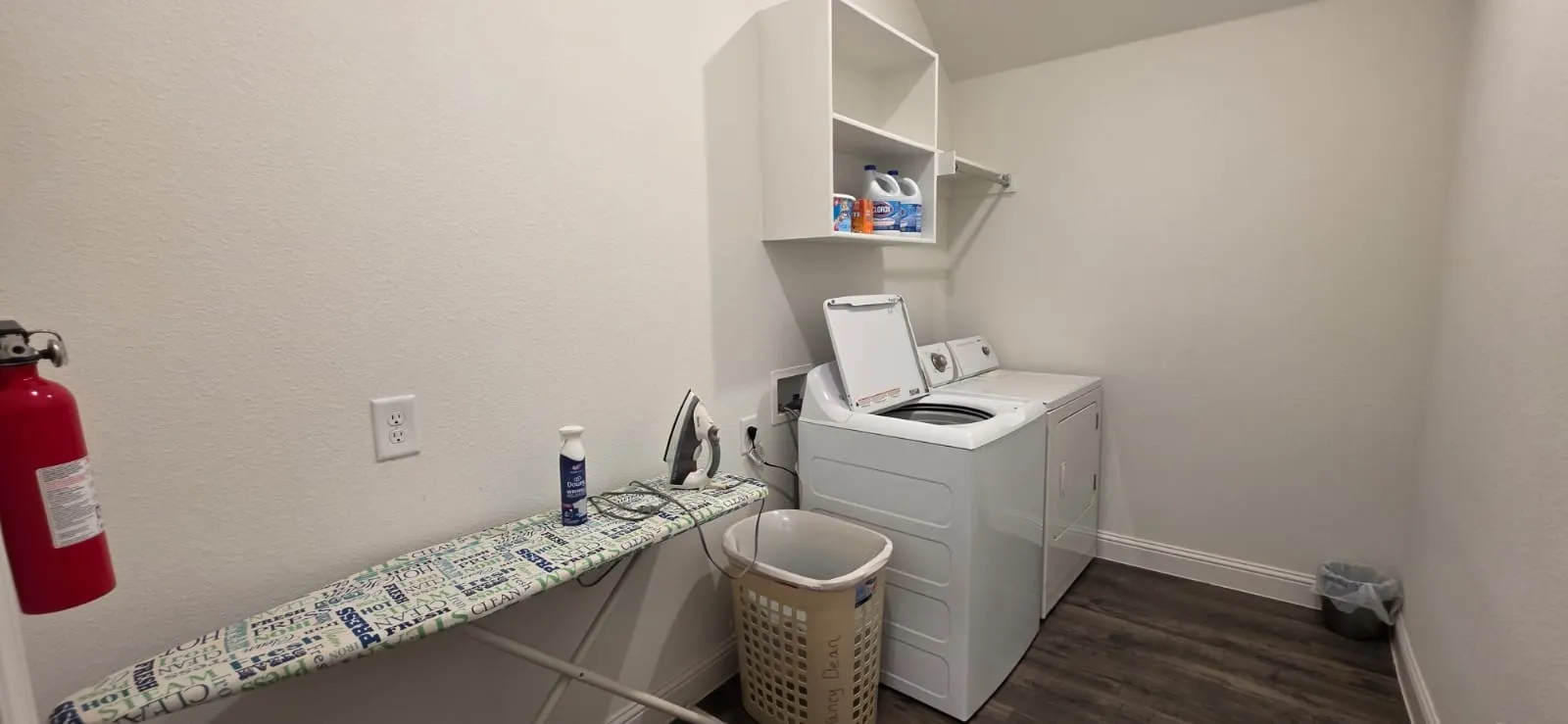 White washer and dryer appliances, wood-finish flooring, and white wall-mounted shelving