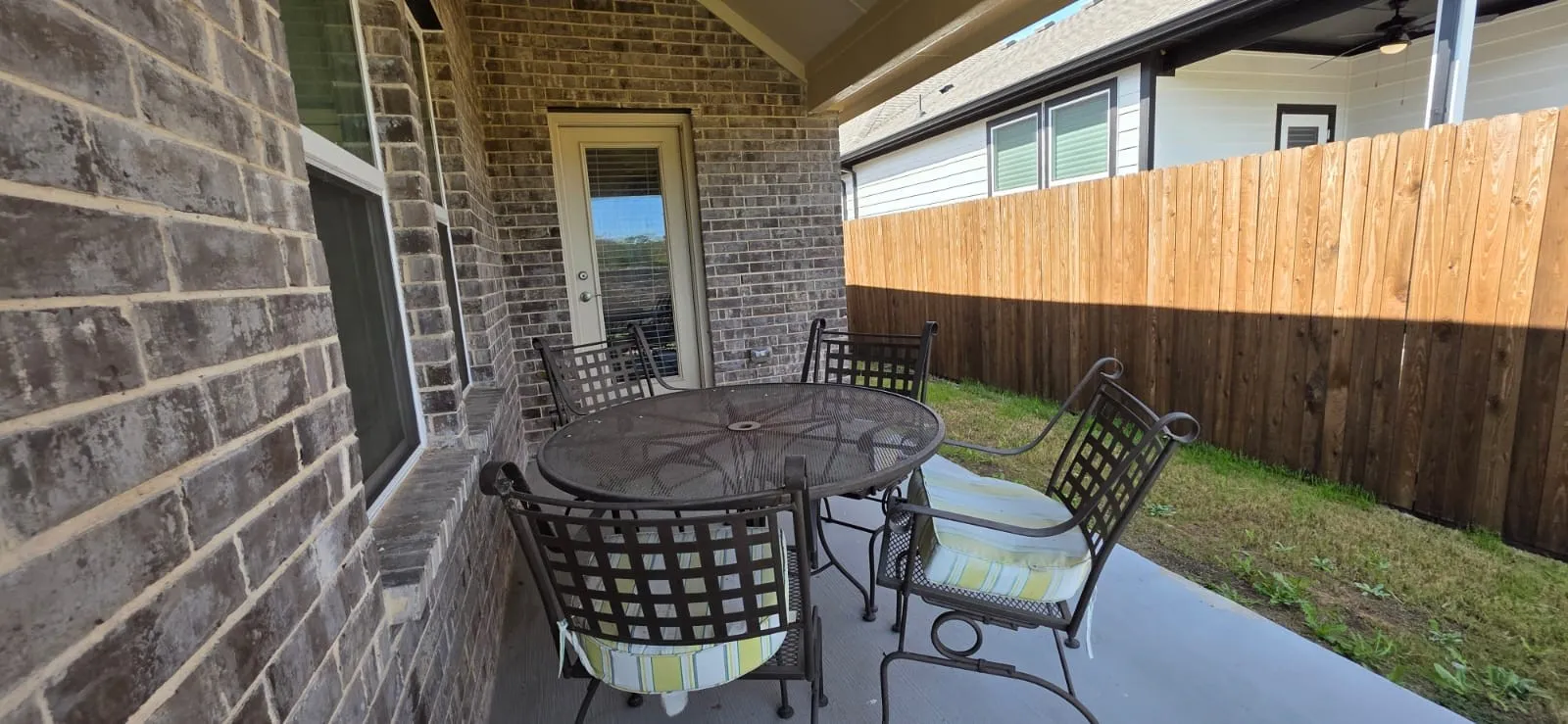 Covered patio with brick siding, a glass-paneled door, and a privacy fence