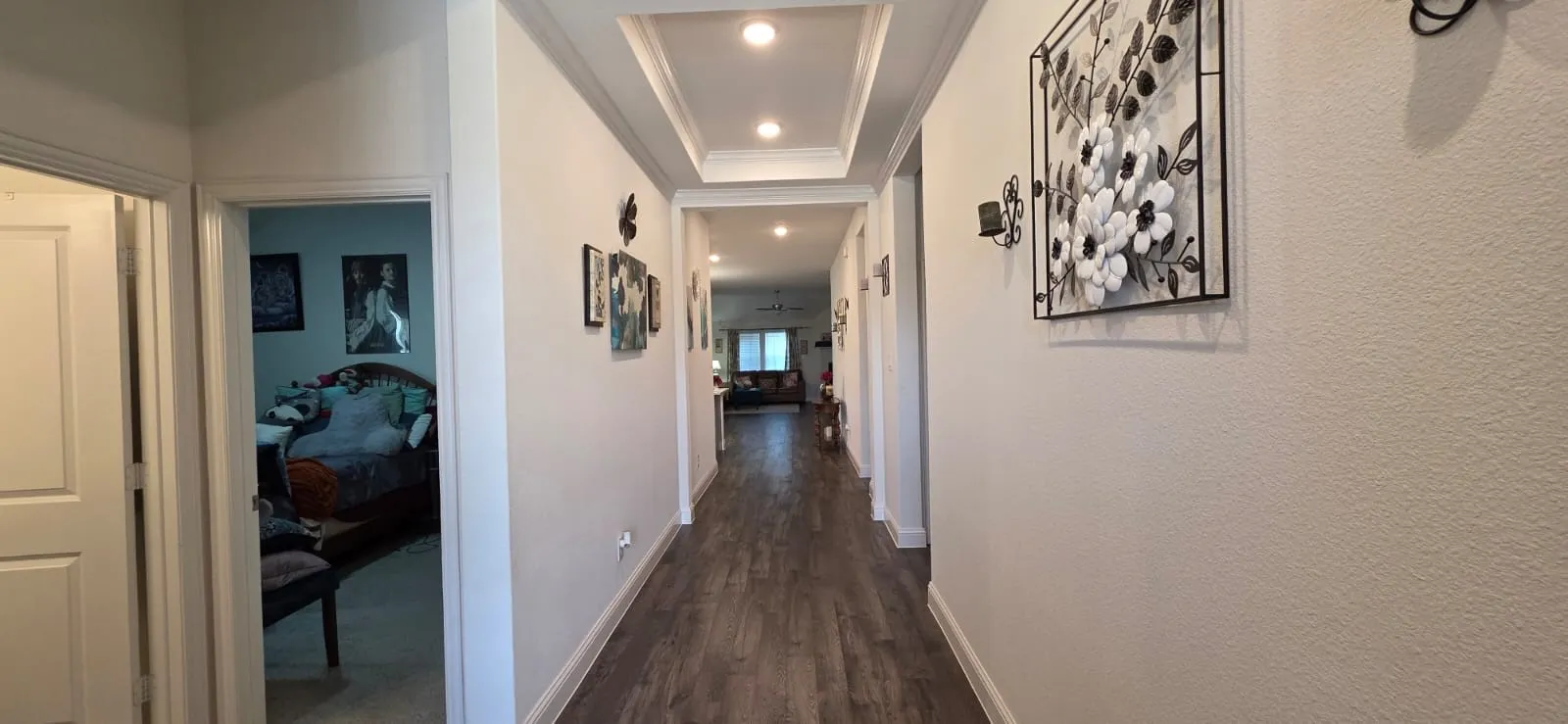 Recessed lighting illuminates a tray ceiling and wood-finish flooring in this hallway