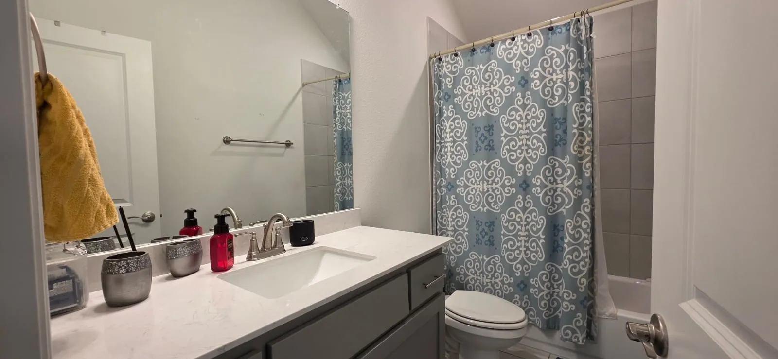 BATH 2 Vanity with an integrated sink and brushed nickel faucet, a large wall-mounted mirror, a toilet, and a tiled shower-tub combination