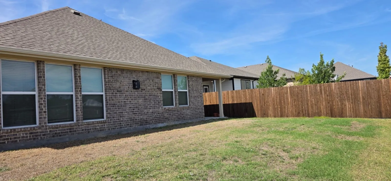 Brick exterior featuring multiple windows with blinds, pitched roof, and a private wooden fence