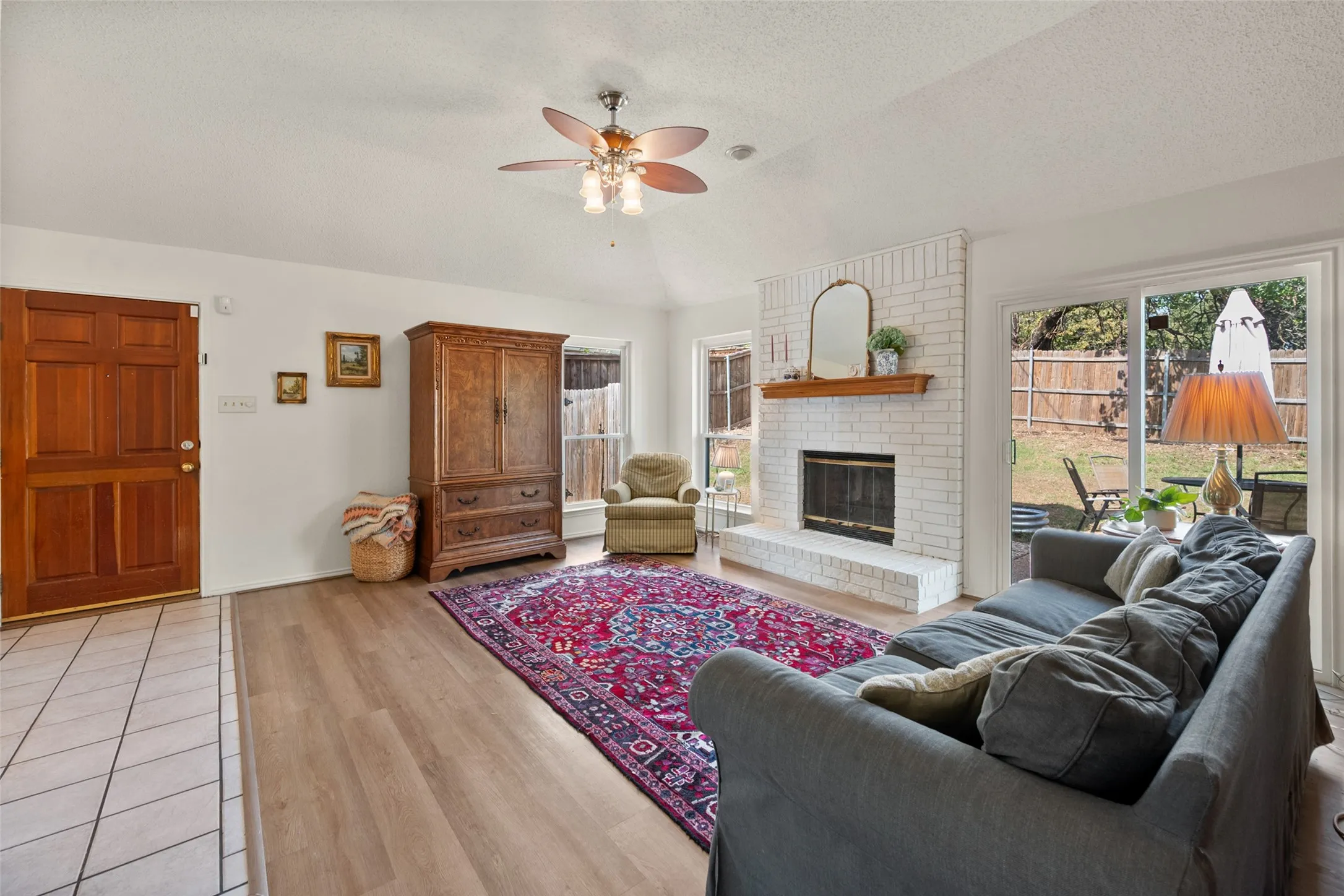 Living area featuring vaulted ceilings, wood-finish flooring, a white brick fireplace with a wood mantel, and sliding glass doors