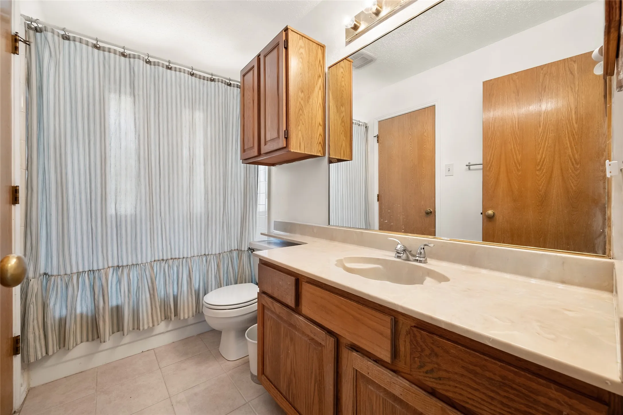 Bathroom featuring a wood-finish vanity with a molded countertop, integrated sink, wall-mounted cabinetry, and a large plate-glass mirror
