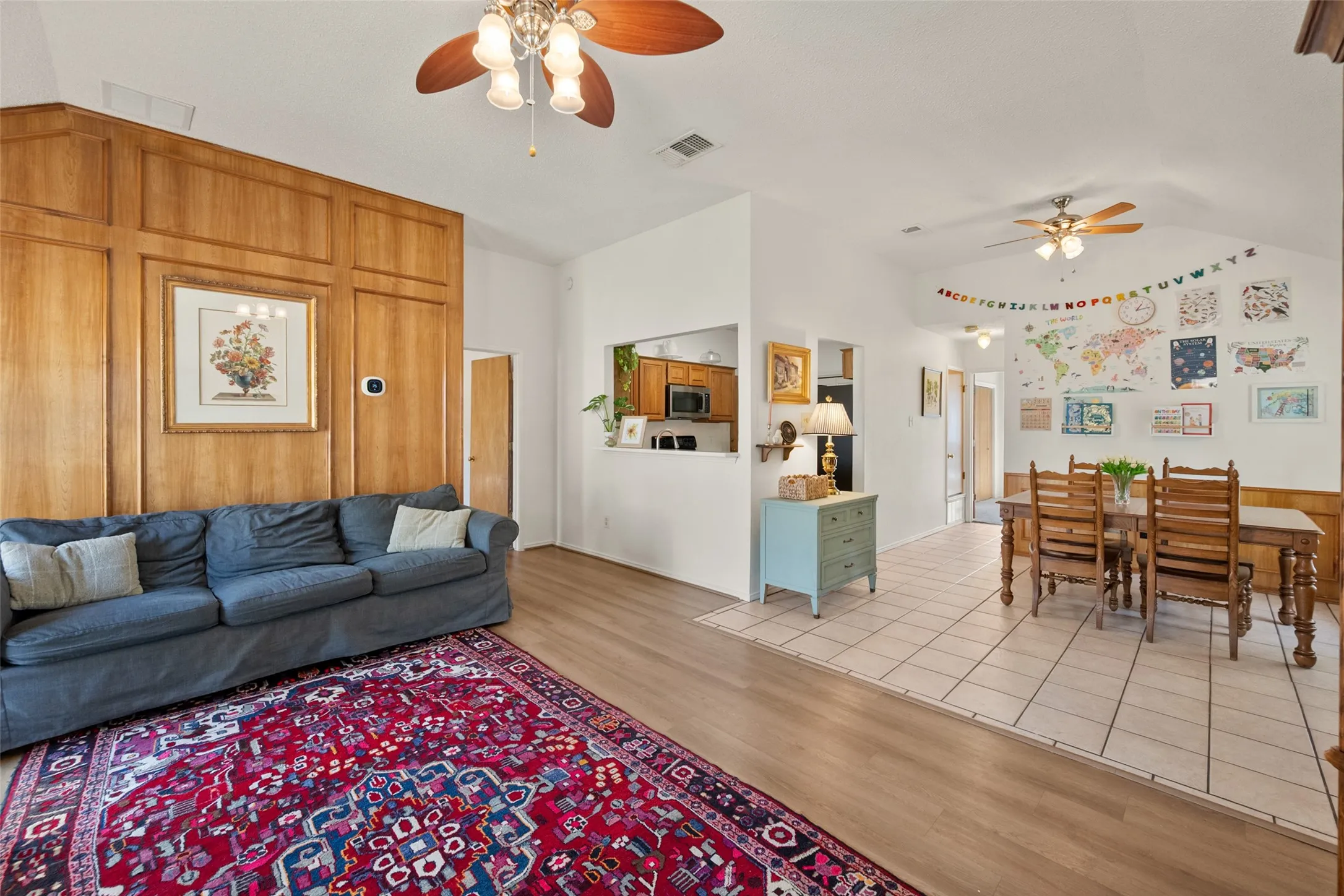 Living area featuring wood-paneled accent wall, vaulted ceilings, dual ceiling fans, and tiled flooring
