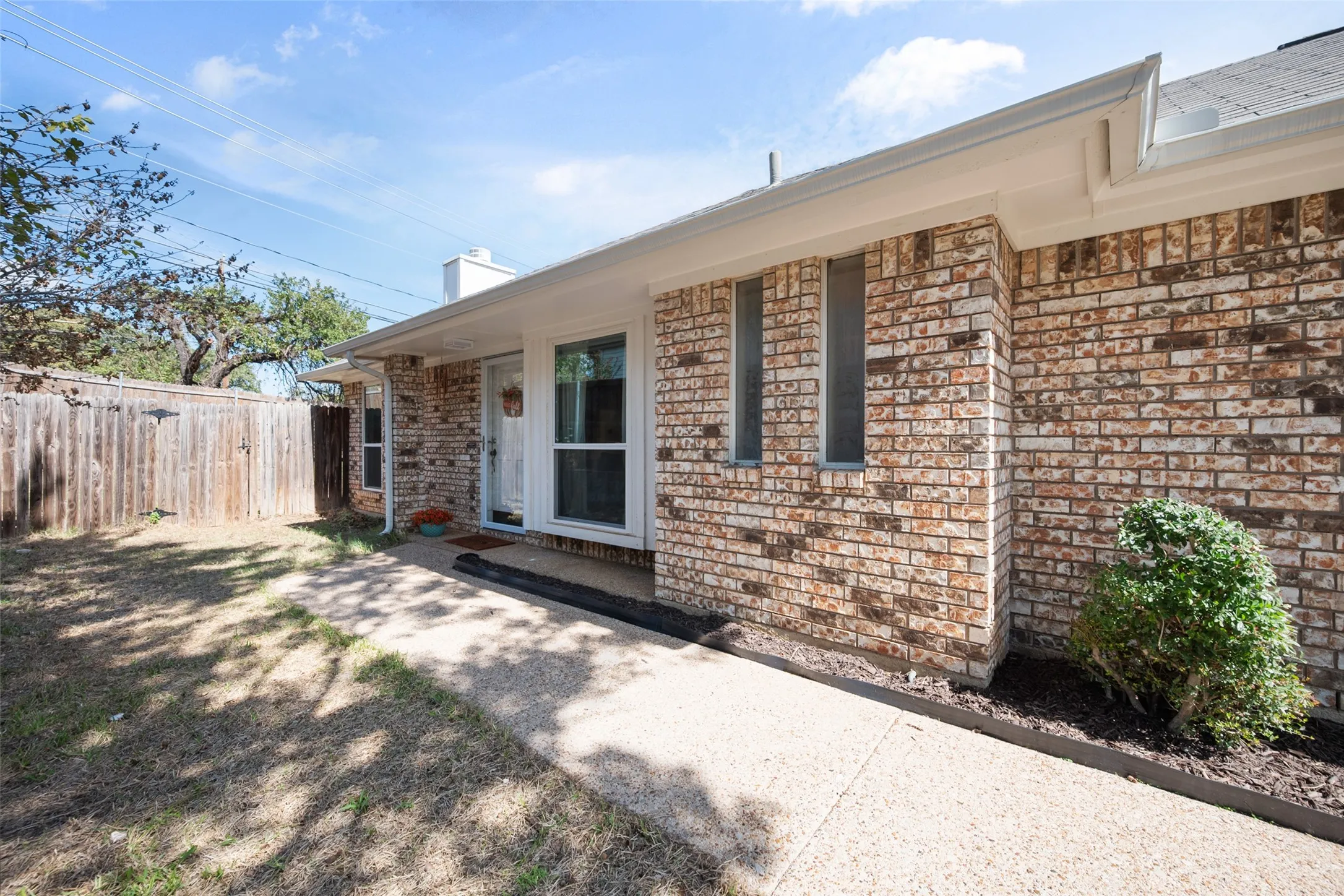 Exterior featuring a brick facade, concrete walkway, vertical windows, and a wood-slat privacy fence