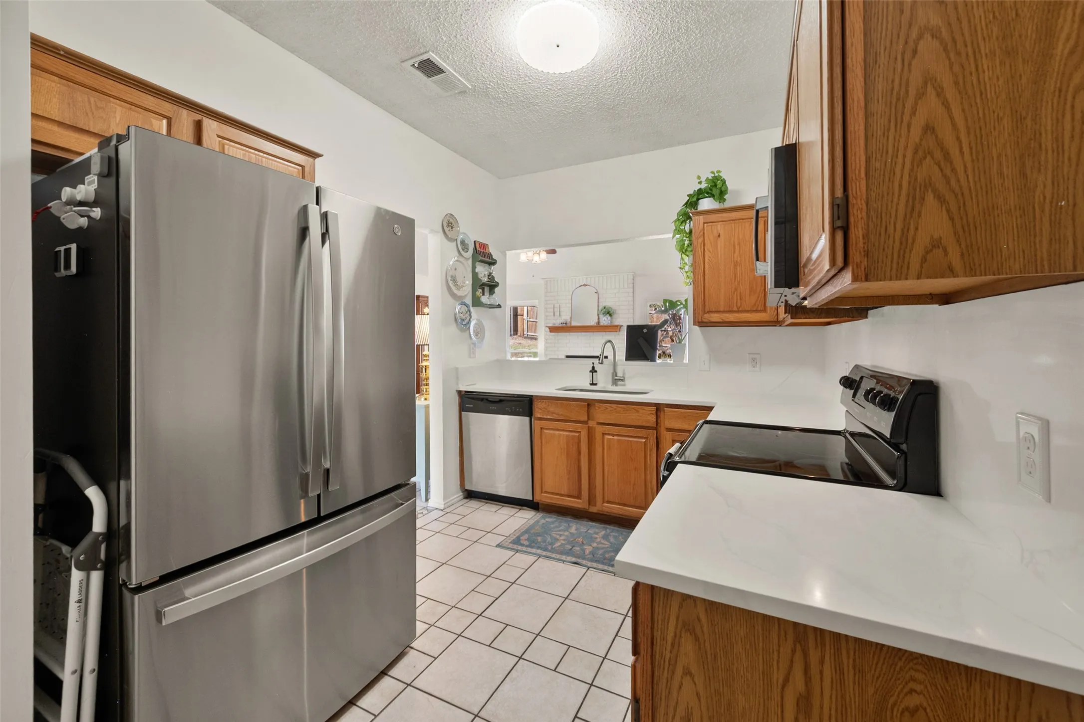 Kitchen featuring stainless steel appliances, wood cabinetry, stone-finish countertops, and ceramic tile flooring