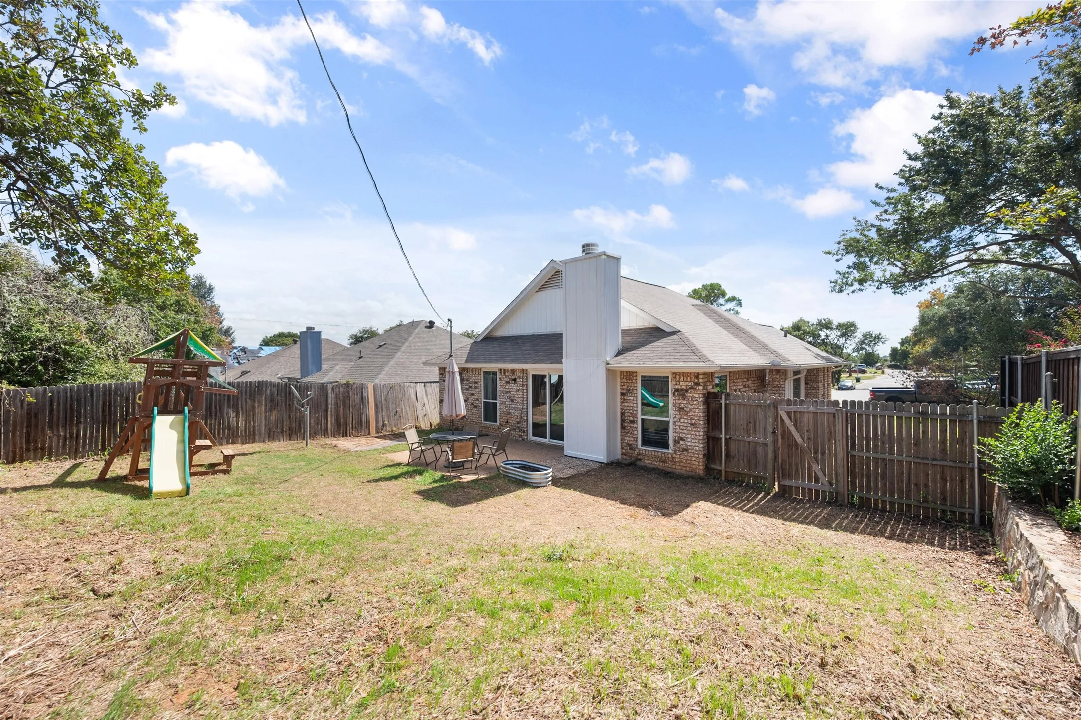 Rear exterior featuring a brick and white siding facade, a paved patio, and a fenced backyard