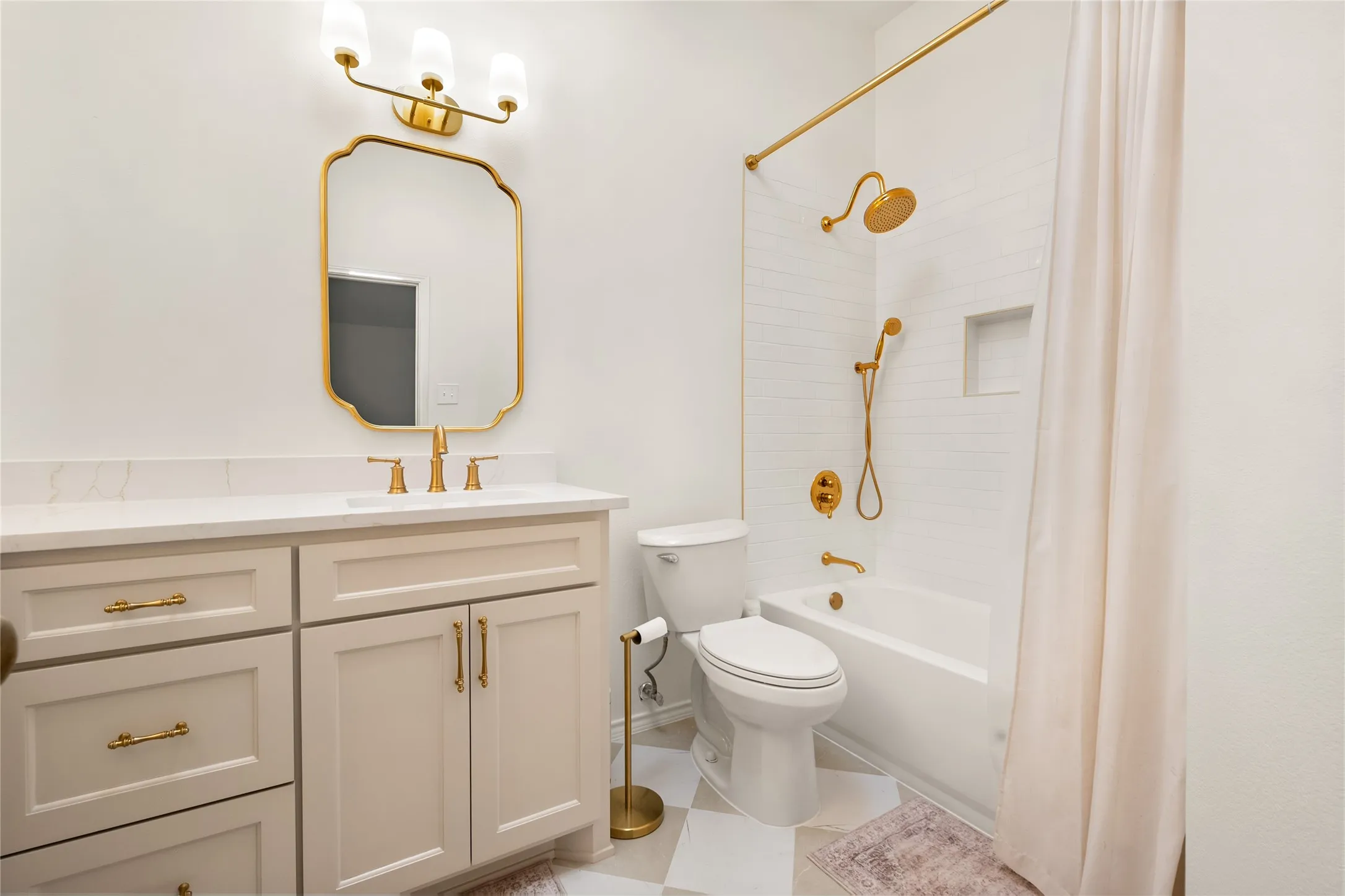 Bathroom featuring a vanity with white stone countertop, gold-toned hardware and fixtures, a custom-shaped mirror, and a tiled tub-shower combination with a built-in recessed niche