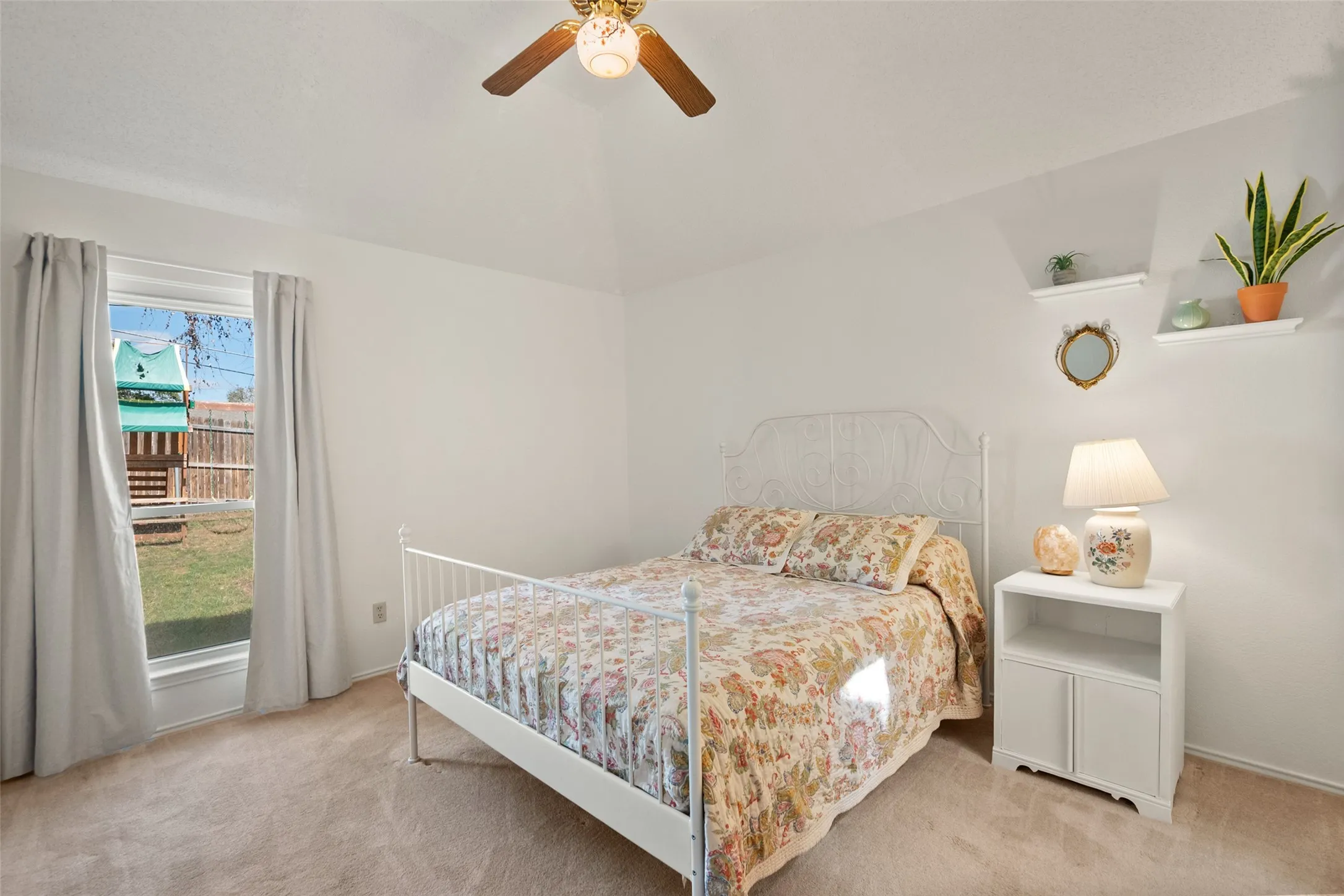 Vaulted ceiling featuring a central ceiling fan, carpeted flooring, and wall-mounted shelving
