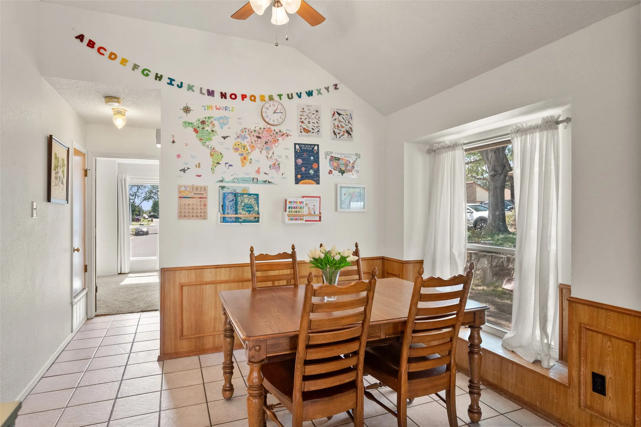 Dining area featuring a vaulted ceiling, wood wainscoting, ceramic tile flooring, and a large window bay