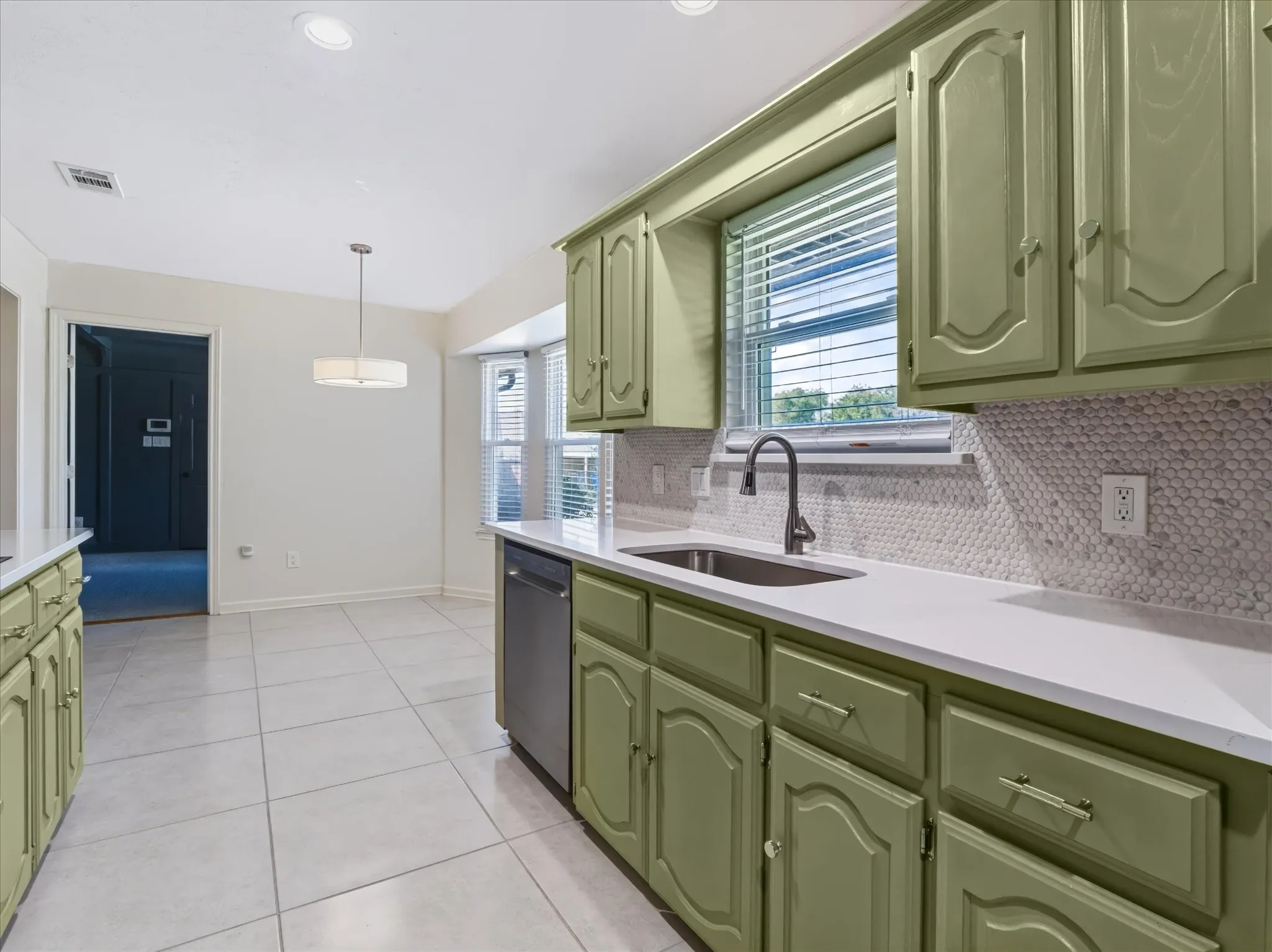 Kitchen featuring custom sage green cabinetry, stone-finish tile flooring, mosaic tile backsplash, solid-surface countertops, and a stainless steel undermount sink with a gooseneck faucet