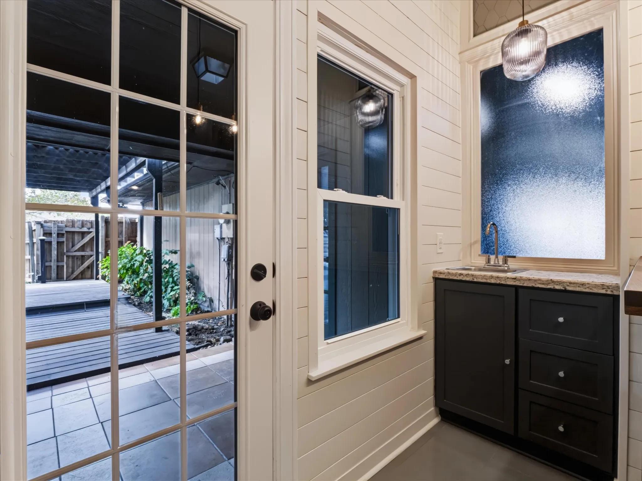 Shiplap wall paneling, built-in cabinetry with a stone countertop and inset sink, glass-paneled exterior door, and pendant lighting