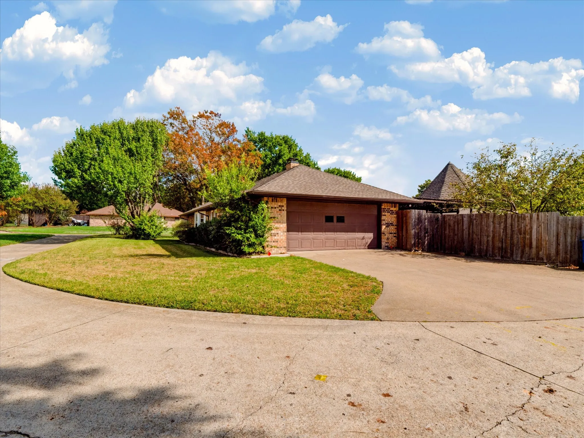 Brick exterior featuring a two-car garage, expansive concrete driveway, and wooden privacy fencing