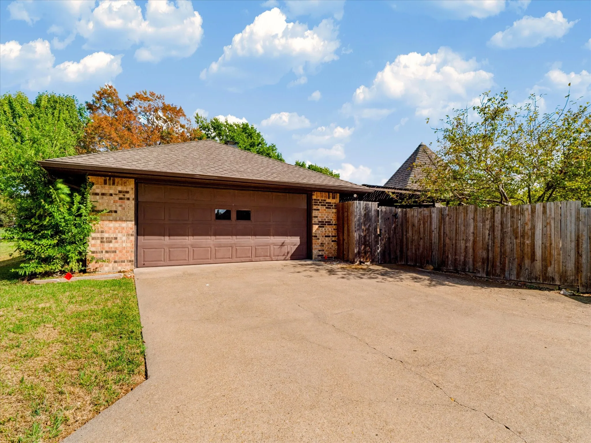 Detached two-car garage featuring brick and siding exterior, concrete driveway, and wooden privacy fencing