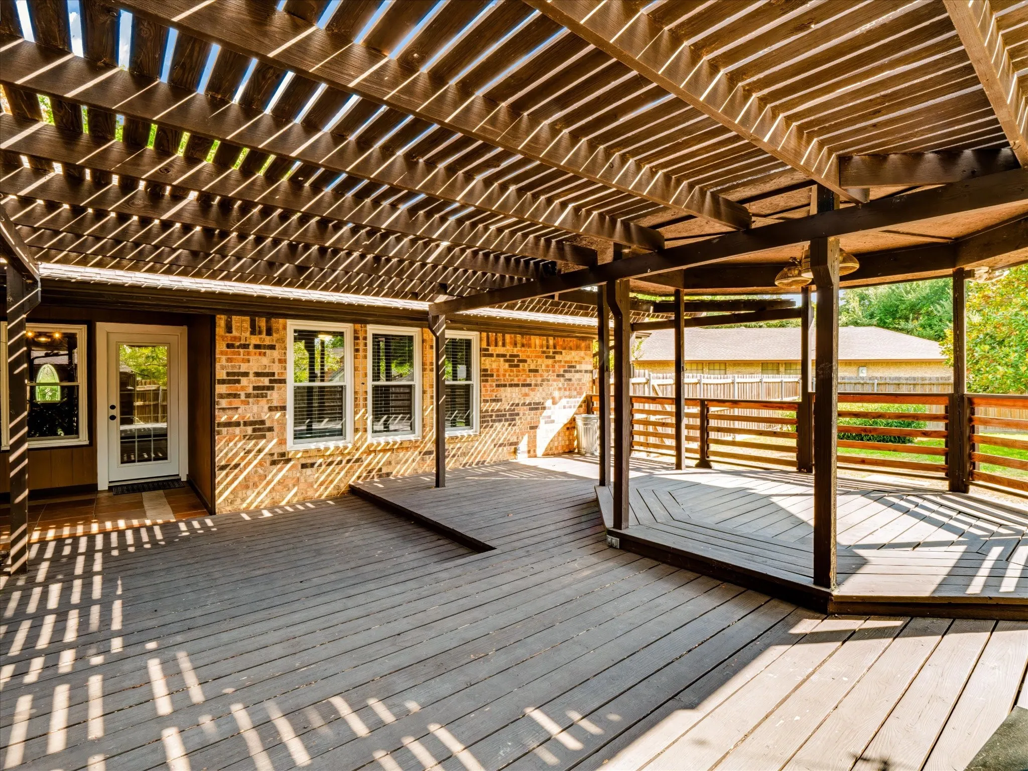 Multi-level wood deck featuring a slatted pergola, hexagonal platform, wood-slat railing, and brick exterior finish