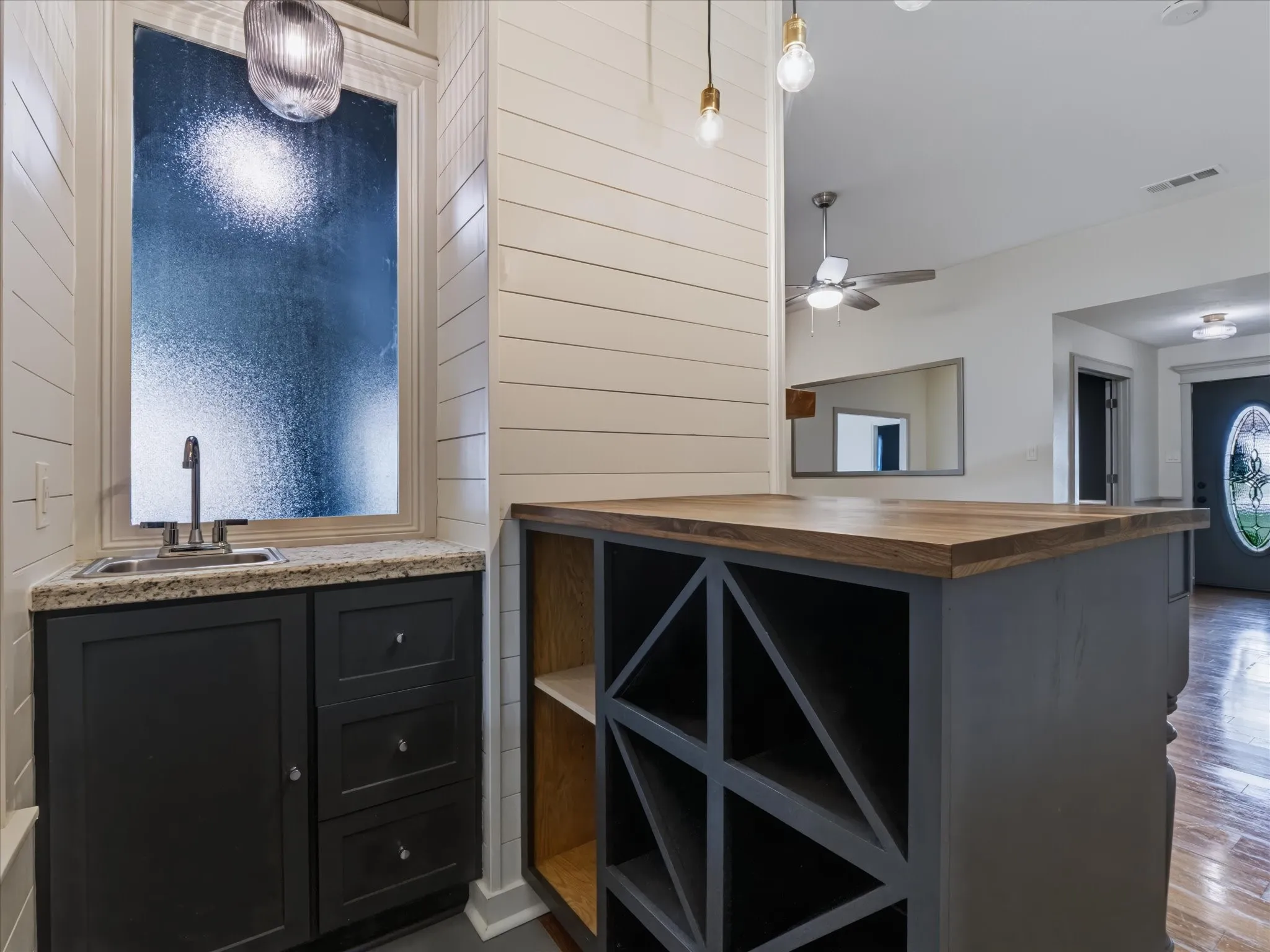Custom built-in bar area featuring shiplap wall paneling, charcoal-toned cabinetry, integrated wine storage, a stone-surface countertop, and a stainless steel drop-in sink