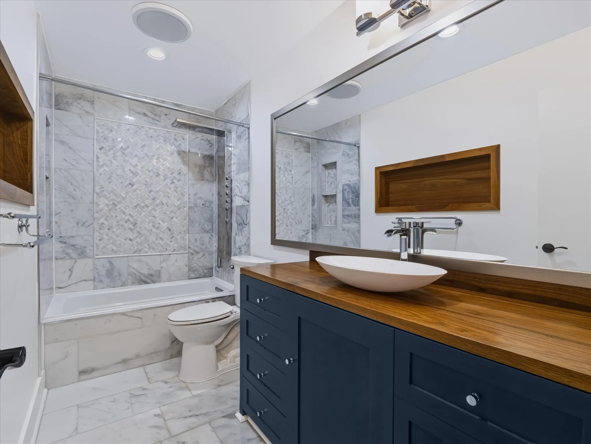 Bathroom featuring a navy blue vanity with a wood countertop, vessel sink, stone-tiled floor, and a walk-in shower with stone surround and herringbone accent inlay