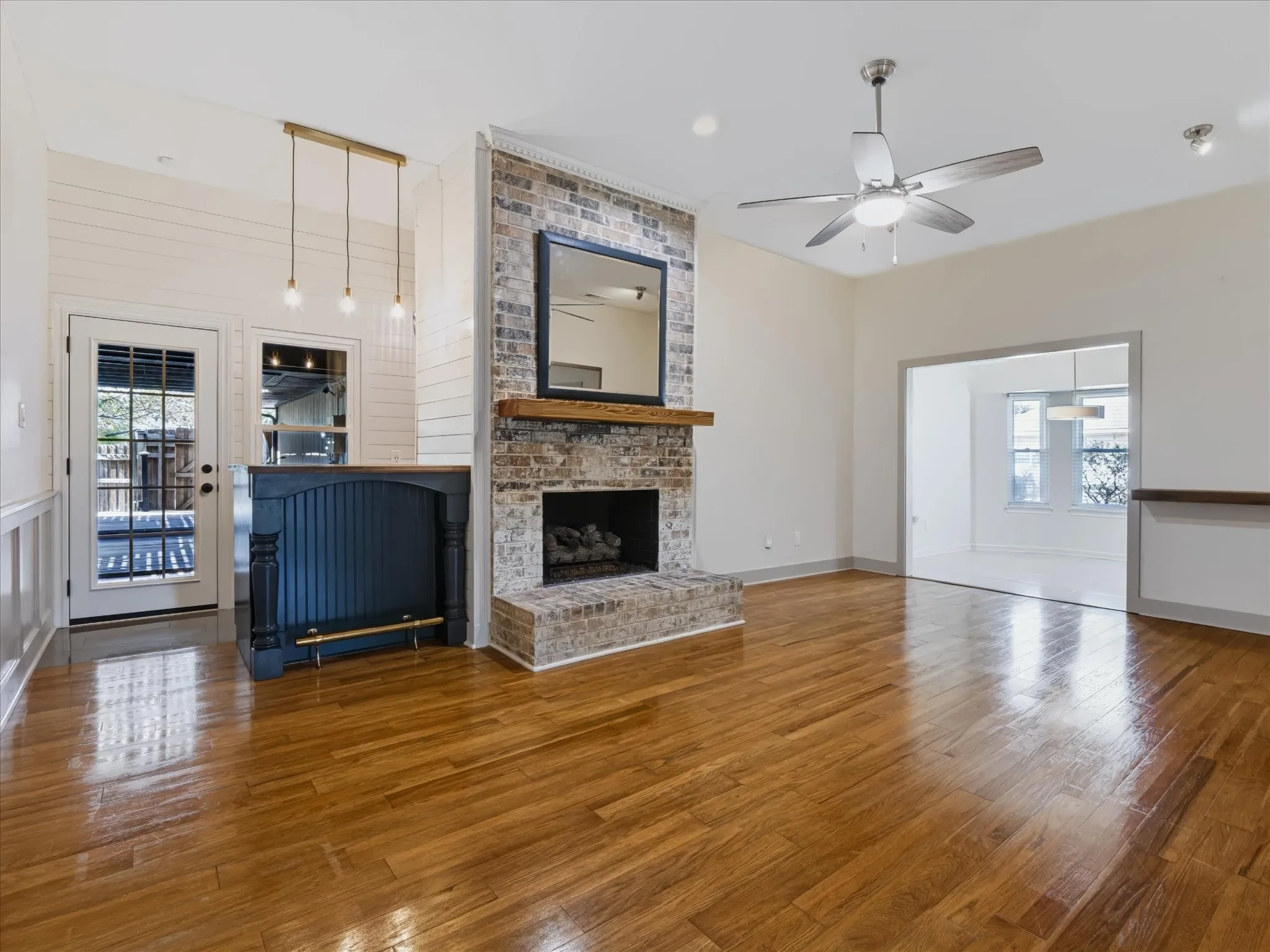 Living area featuring wood-finish flooring, a floor-to-ceiling brick fireplace with a wood mantel, a built-in wet bar, shiplap wall accents, and a ceiling fan