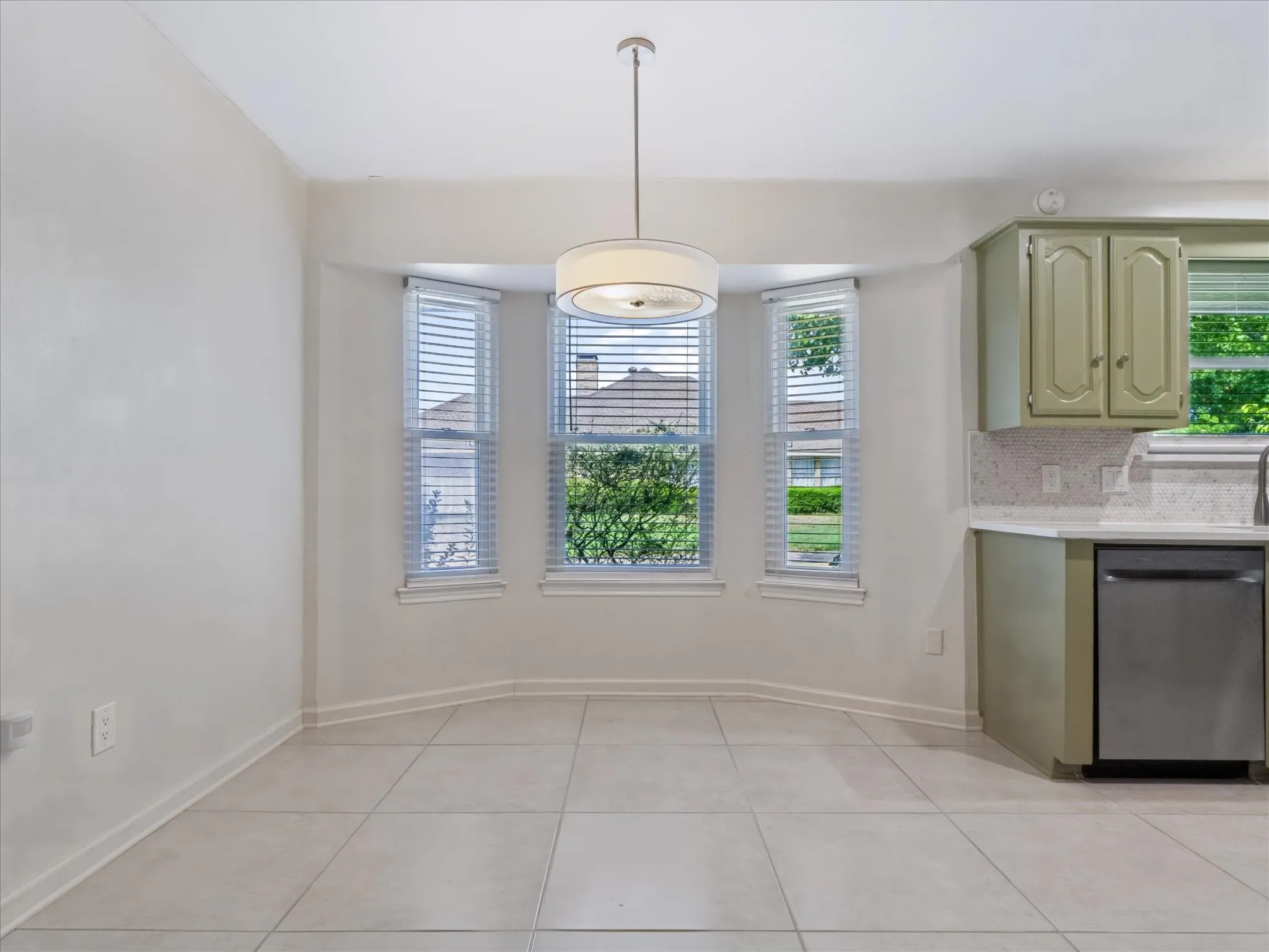 Bay window with three paneled windows, tile flooring, drum-style pendant light fixture, cabinetry with recessed panel doors, and solid-surface countertops