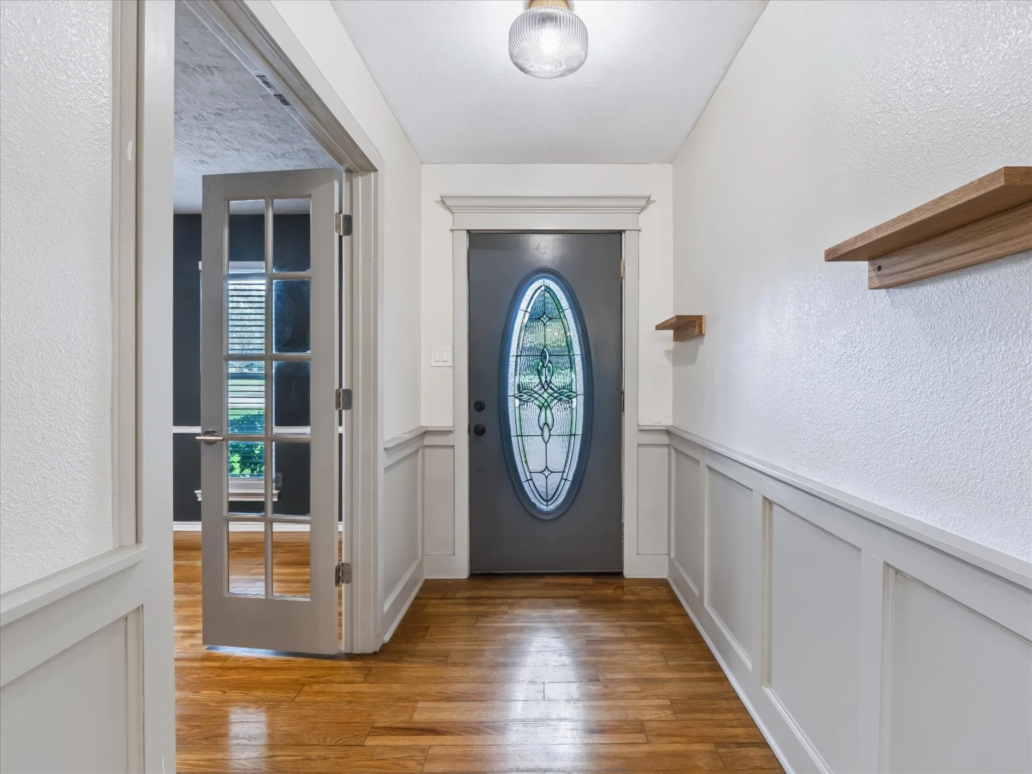 Entryway featuring wood-finish flooring, wainscoting, a door with an oval decorative glass insert, and built-in wall-mounted shelving