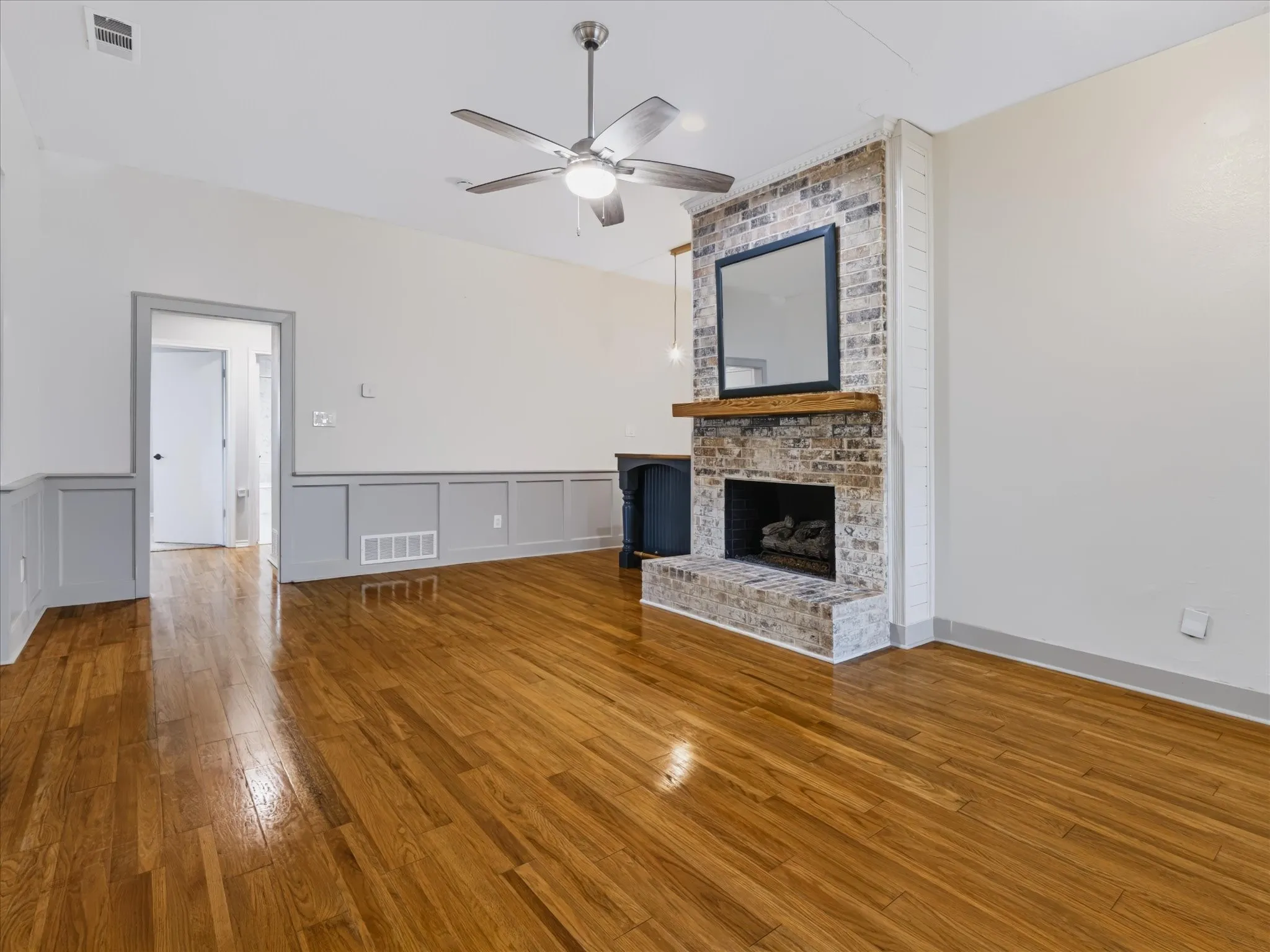 Living space featuring wood-finish flooring, a floor-to-ceiling brick fireplace with a wood mantel, and wainscoting detail
