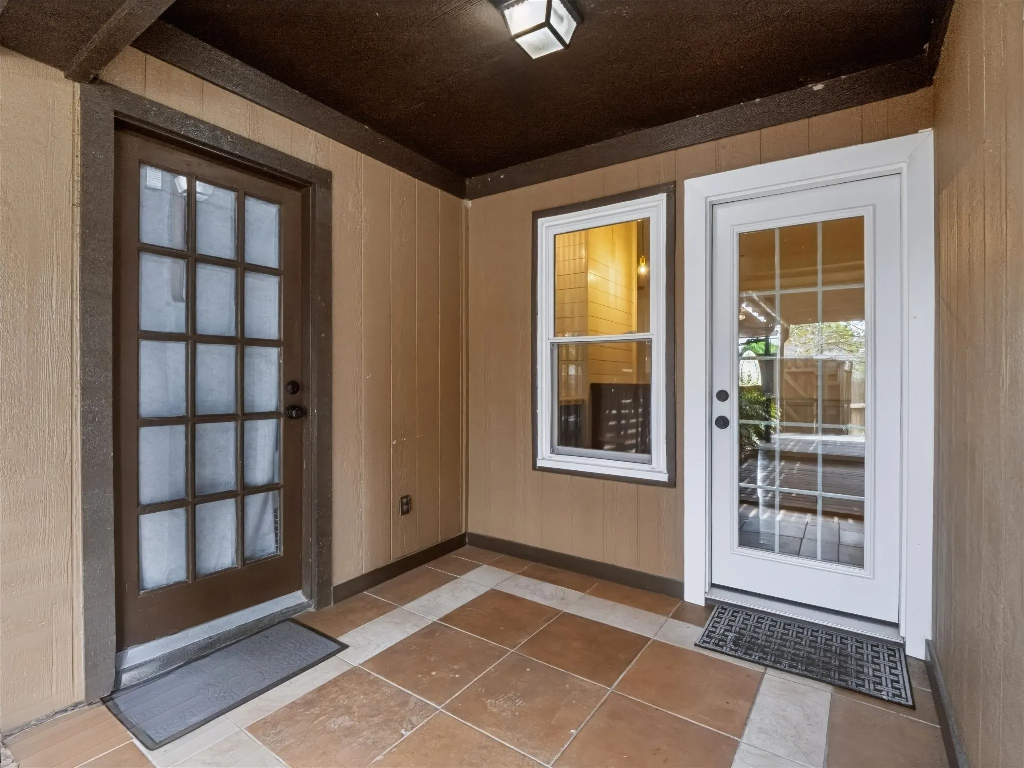 Covered entryway featuring large-format ceramic tile flooring, a multi-pane glass entry door, a secondary glass-panel door, and a single-hung window with a white frame