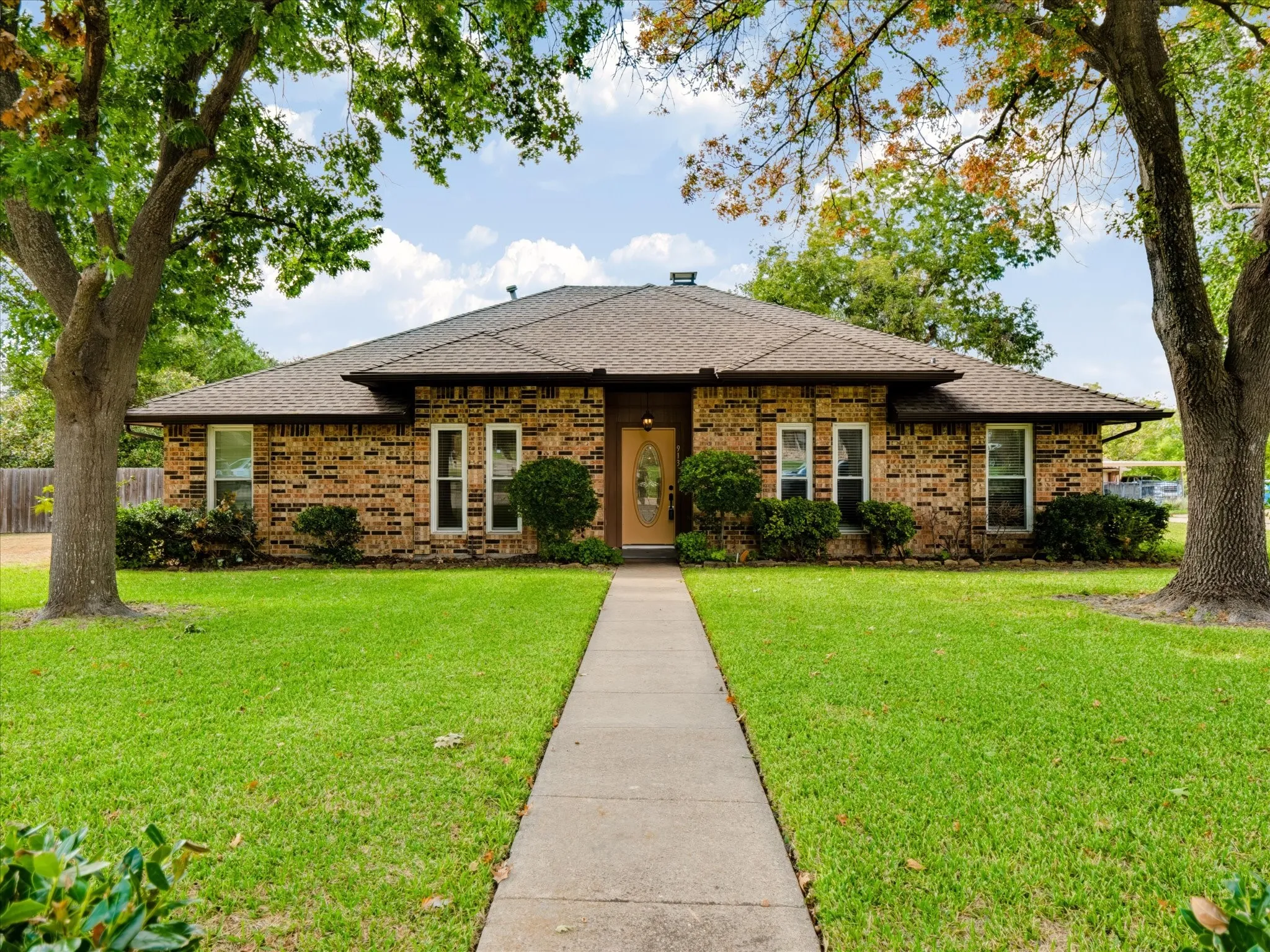 Single-story residence with a brick exterior, hipped roof, centered entryway, and mature trees on a landscaped lot