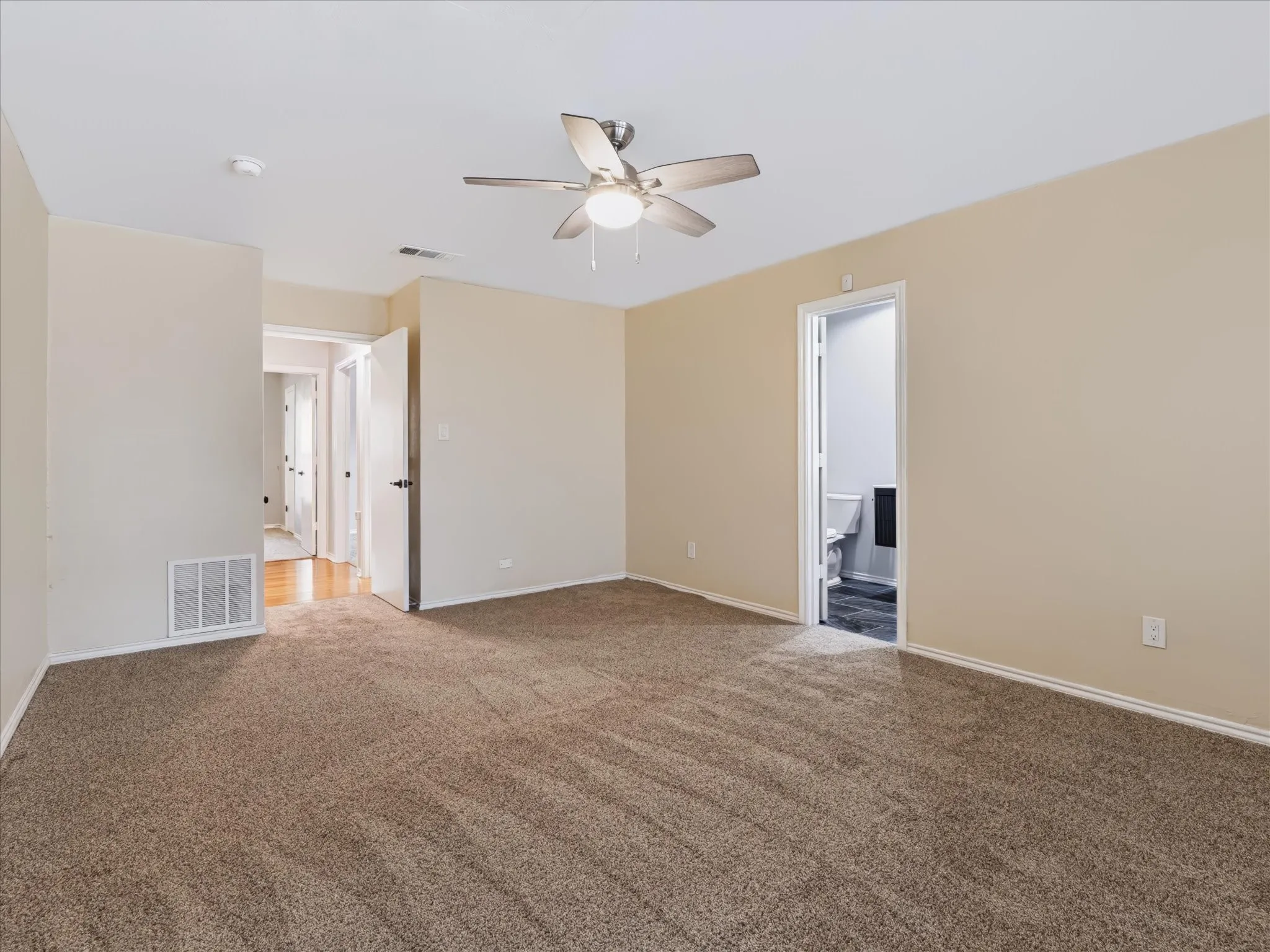 Neutral-toned room featuring wall-to-wall carpeting, a ceiling-mounted light fixture with fan, and solid-core interior doors