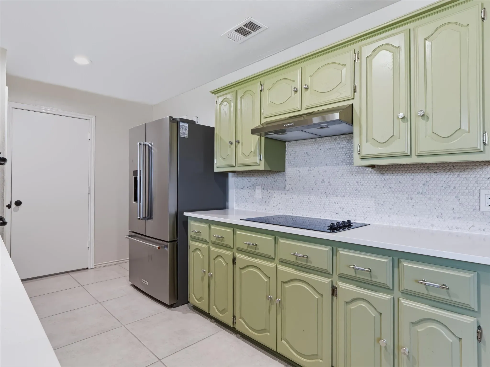 Kitchen featuring sage green raised-panel cabinetry, white solid-surface countertops, a hexagonal tile backsplash, stainless steel French door refrigerator, and a flush-mounted induction cooktop