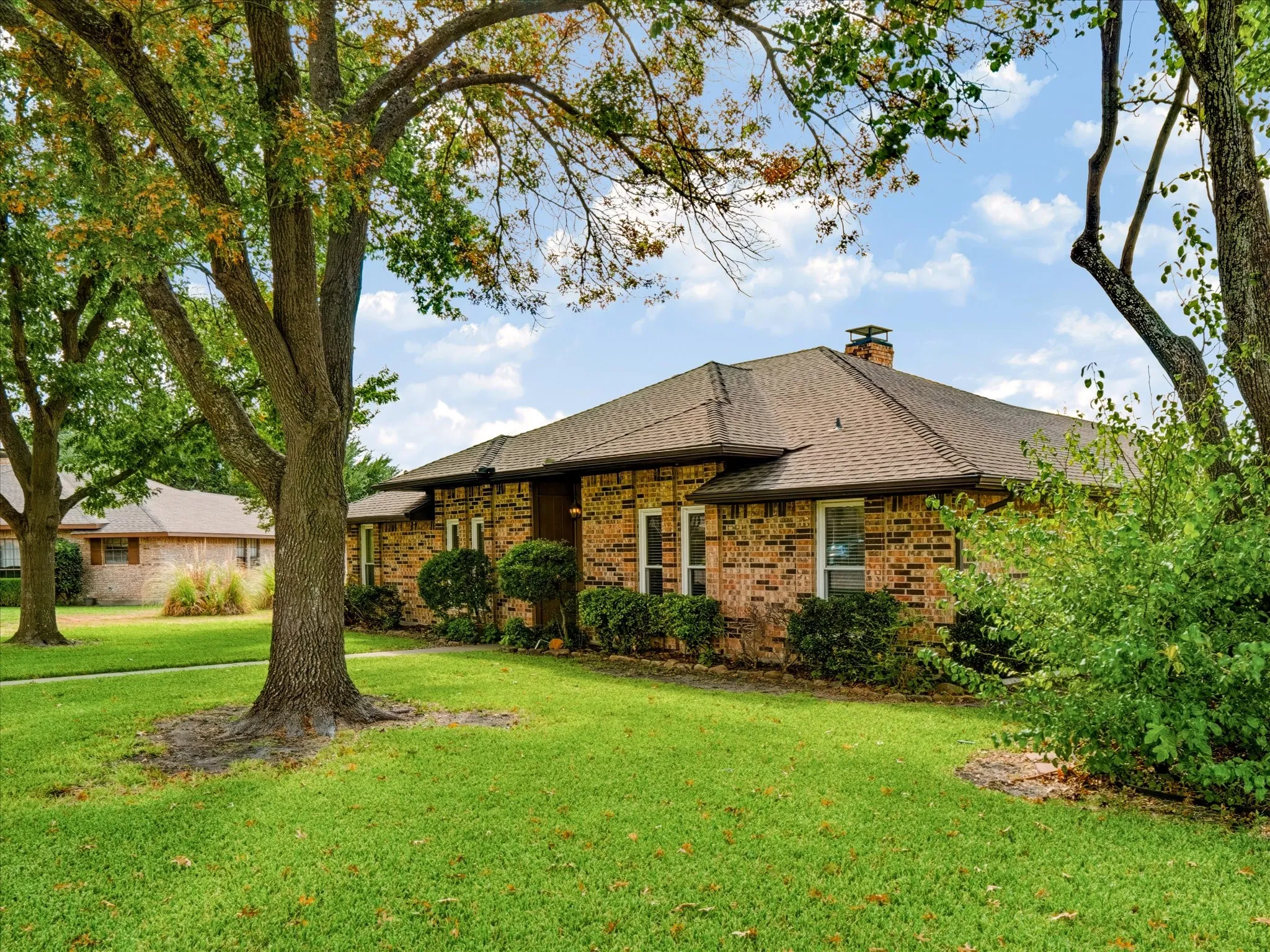 Single-story brick exterior featuring a multi-gable roofline, a chimney, and mature trees on a landscaped lot