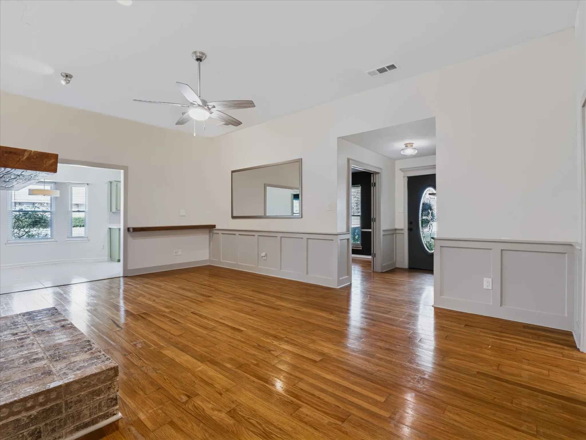 Living space featuring high ceilings, wood-finish flooring, wainscoting, a brick fireplace hearth, and a ceiling fan with integrated lighting