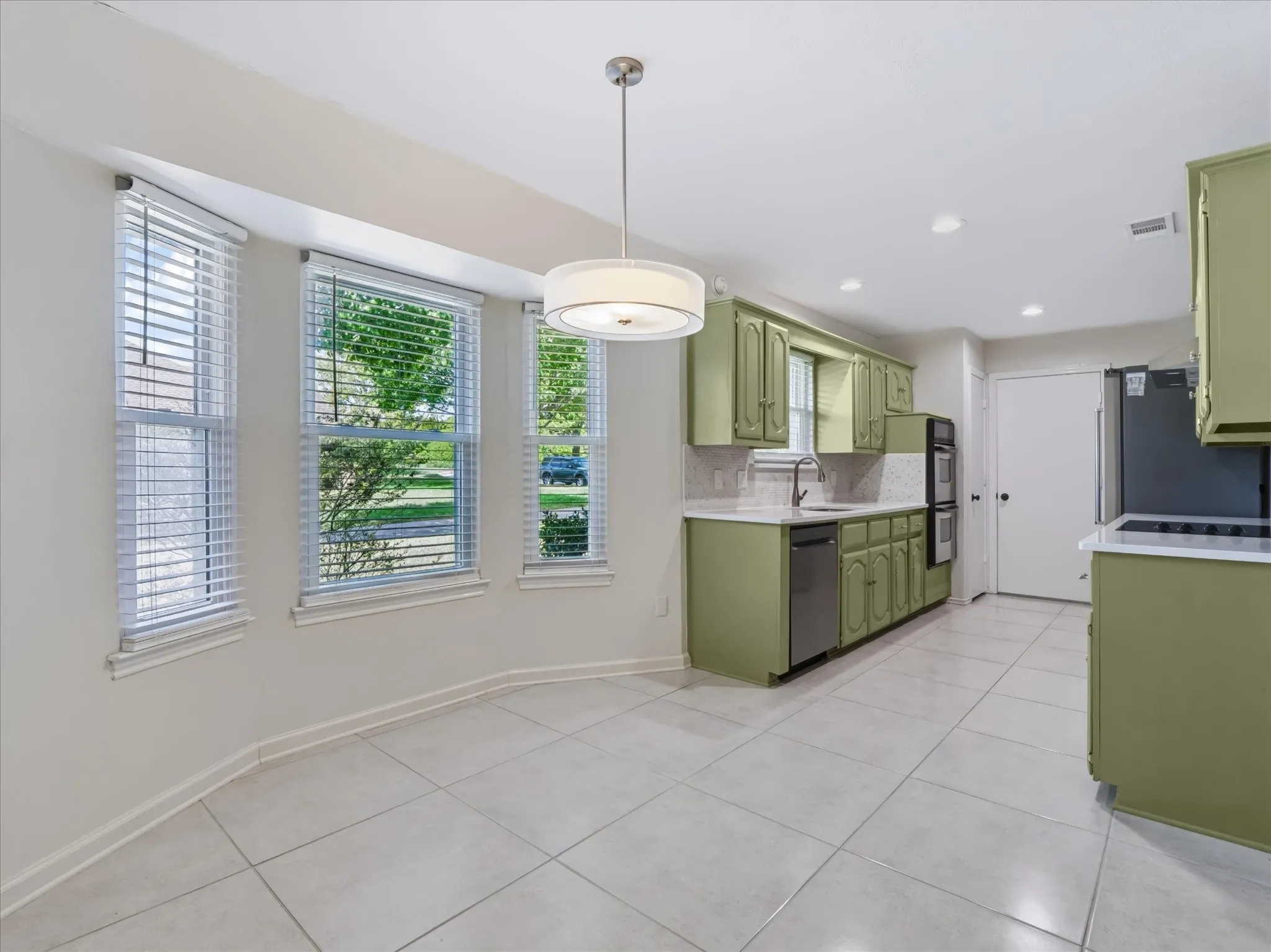 Kitchen featuring light-toned tile flooring, bay windows with horizontal blinds, integrated cabinetry, recessed lighting, and a drum-style pendant light