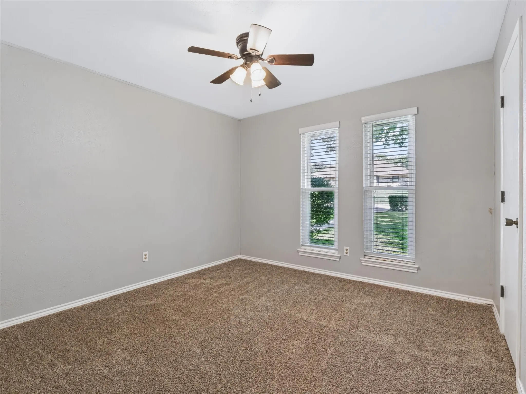 Neutral-toned interior room featuring wall-to-wall carpeting, dual windows with blinds, and a multi-blade ceiling fan with integrated light fixture