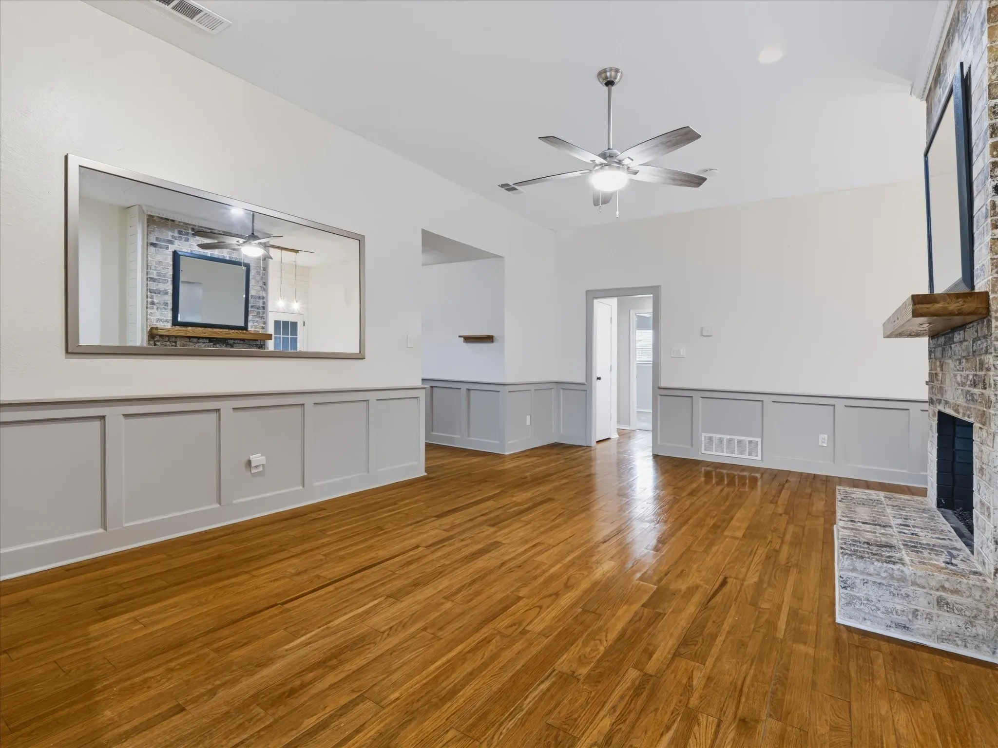 Living area featuring wood-finish flooring, wainscoting, vaulted ceilings, and a fireplace with a masonry surround and timber mantel