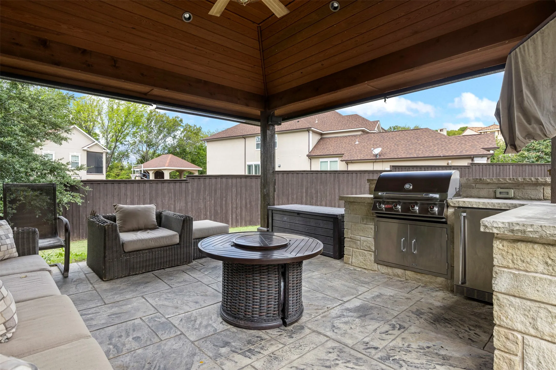 Covered patio featuring a stained wood-plank ceiling, recessed lighting, outdoor kitchen with stainless steel grill, stone-finish masonry, and stamped concrete flooring