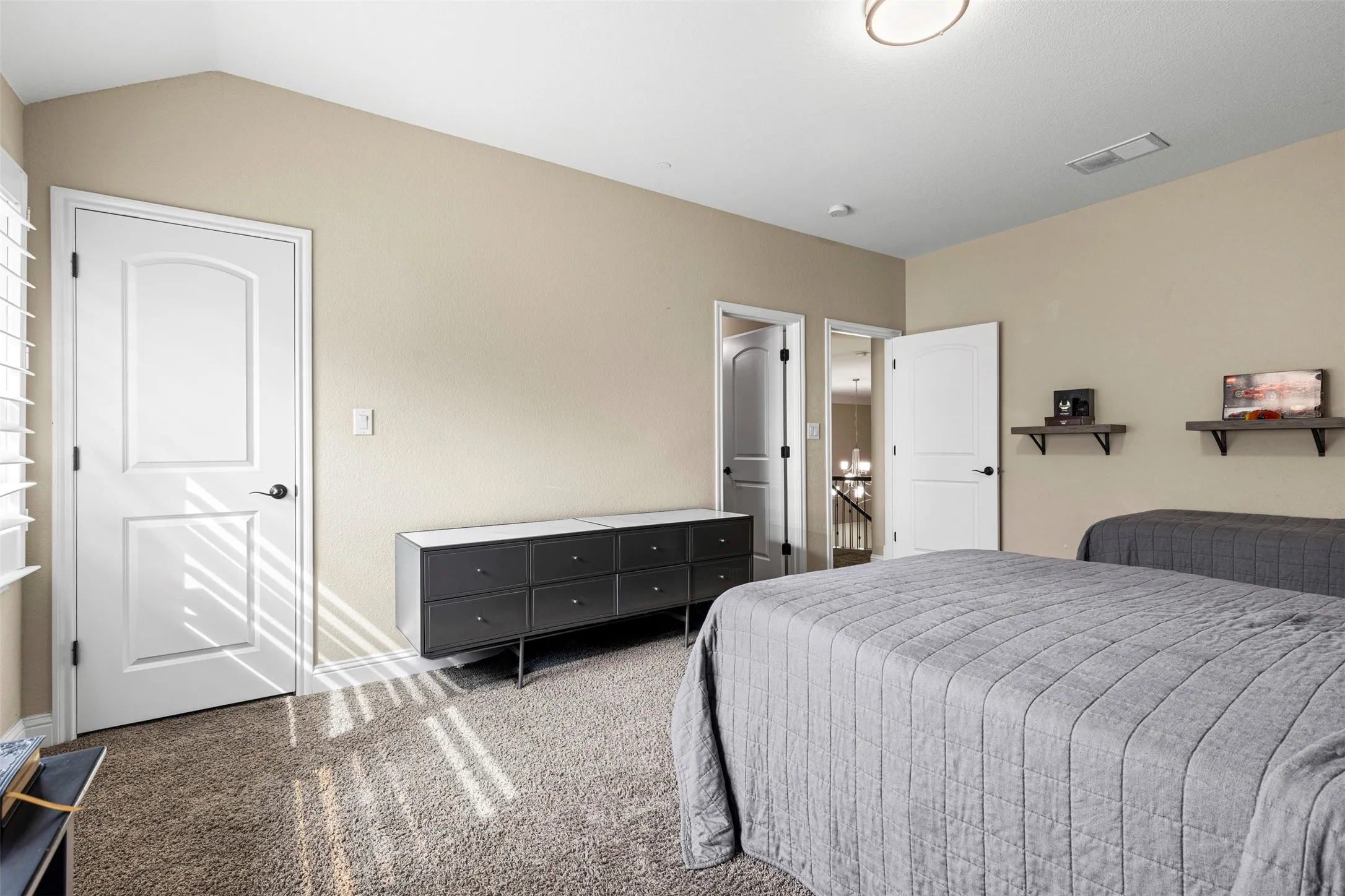 Vaulted ceilings, neutral wall tones, carpeted flooring, two interior panel doors, and wall-mounted floating shelves