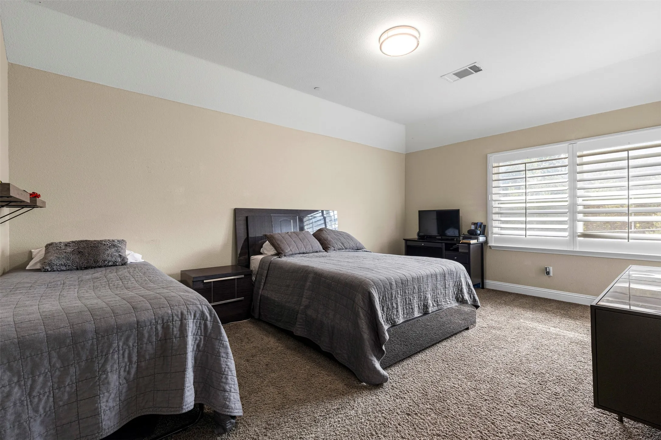Room featuring high ceilings, wall-to-wall carpeting, and windows fitted with white plantation shutters
