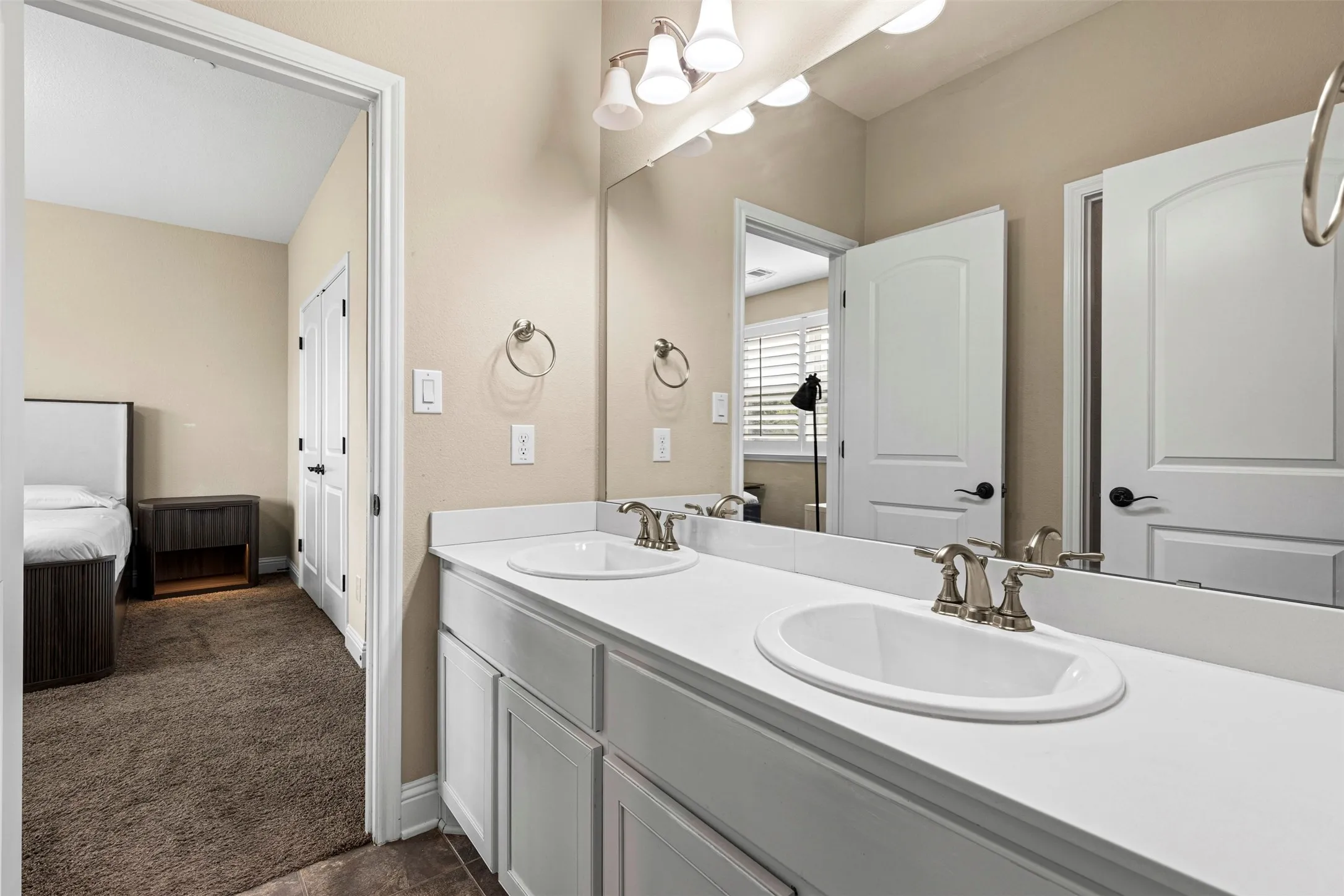 Dual-vanity bathroom featuring white cabinetry, a solid-surface countertop with integrated basins, brushed nickel hardware, and a full-width wall mirror